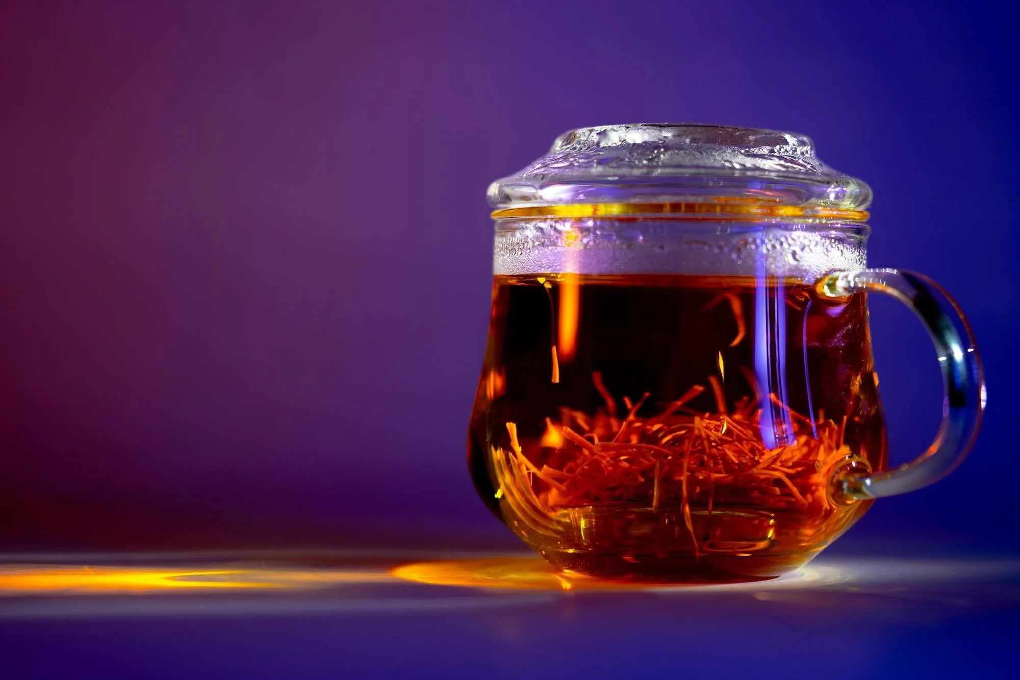 A glass mug of infused saffron-water on a purple background