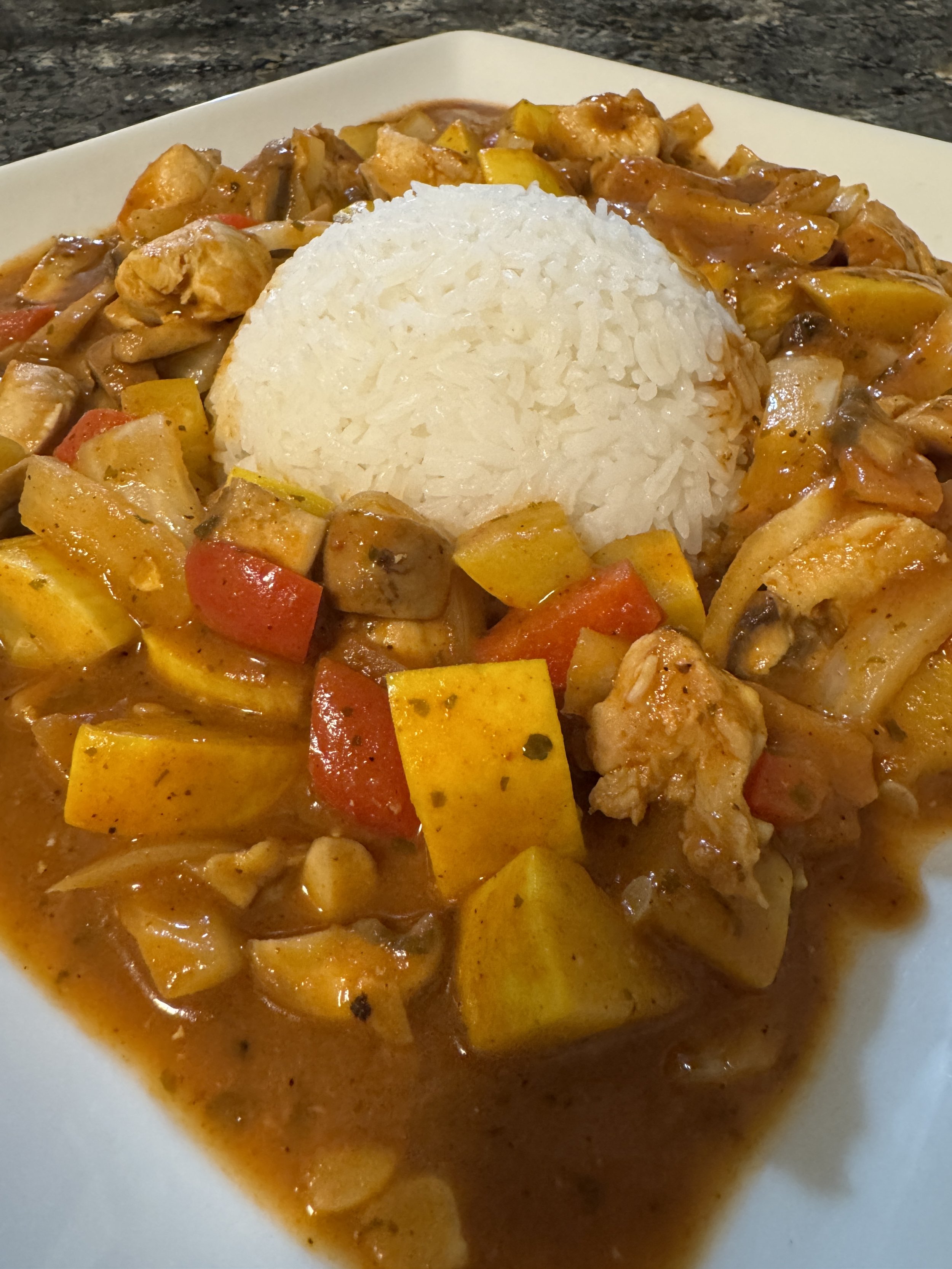 A warm, golden-yellow chicken curry rich with turmeric and spices, neatly arranged around a center-molded dome of white jasmine rice and topped with colorful roasted squash.