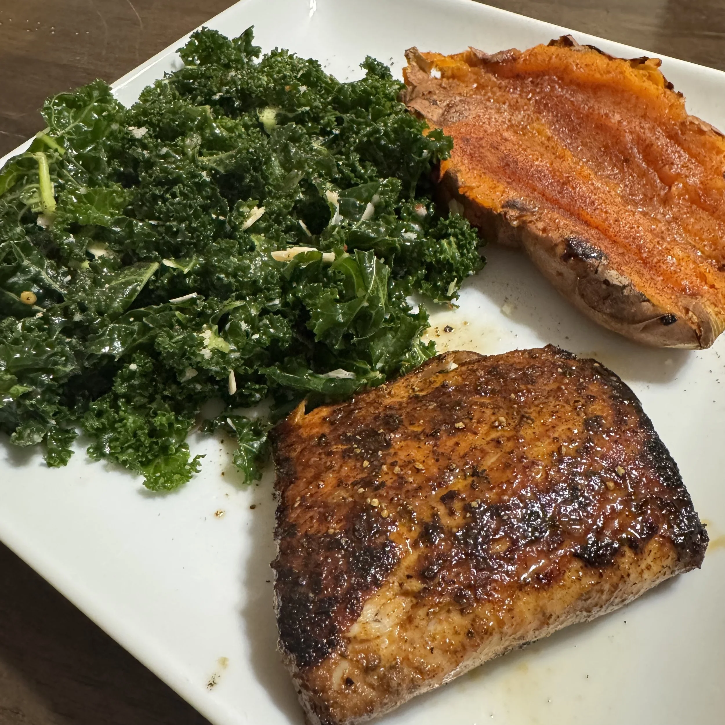 A golden-seared mahi-mahi fillet served with a half-baked sweet potato and a generous side of dark green, massaged kale salad tossed with light dressing.