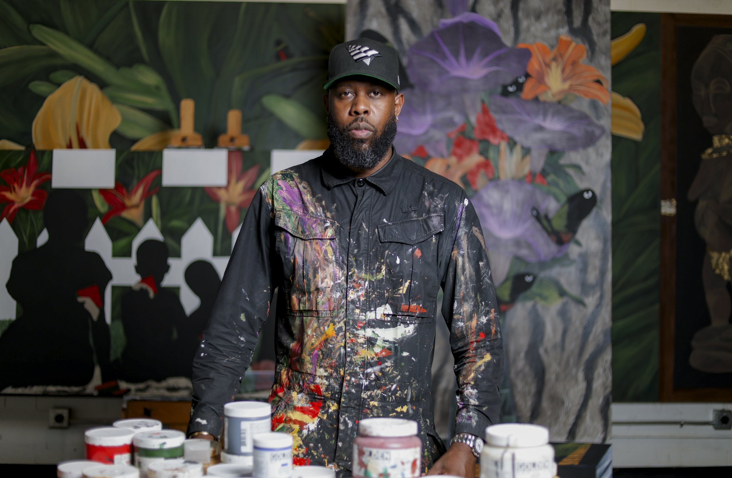 Artist with acrylic paint on his jumpsuit. Behind him his art paintings in his studio, in Dallas