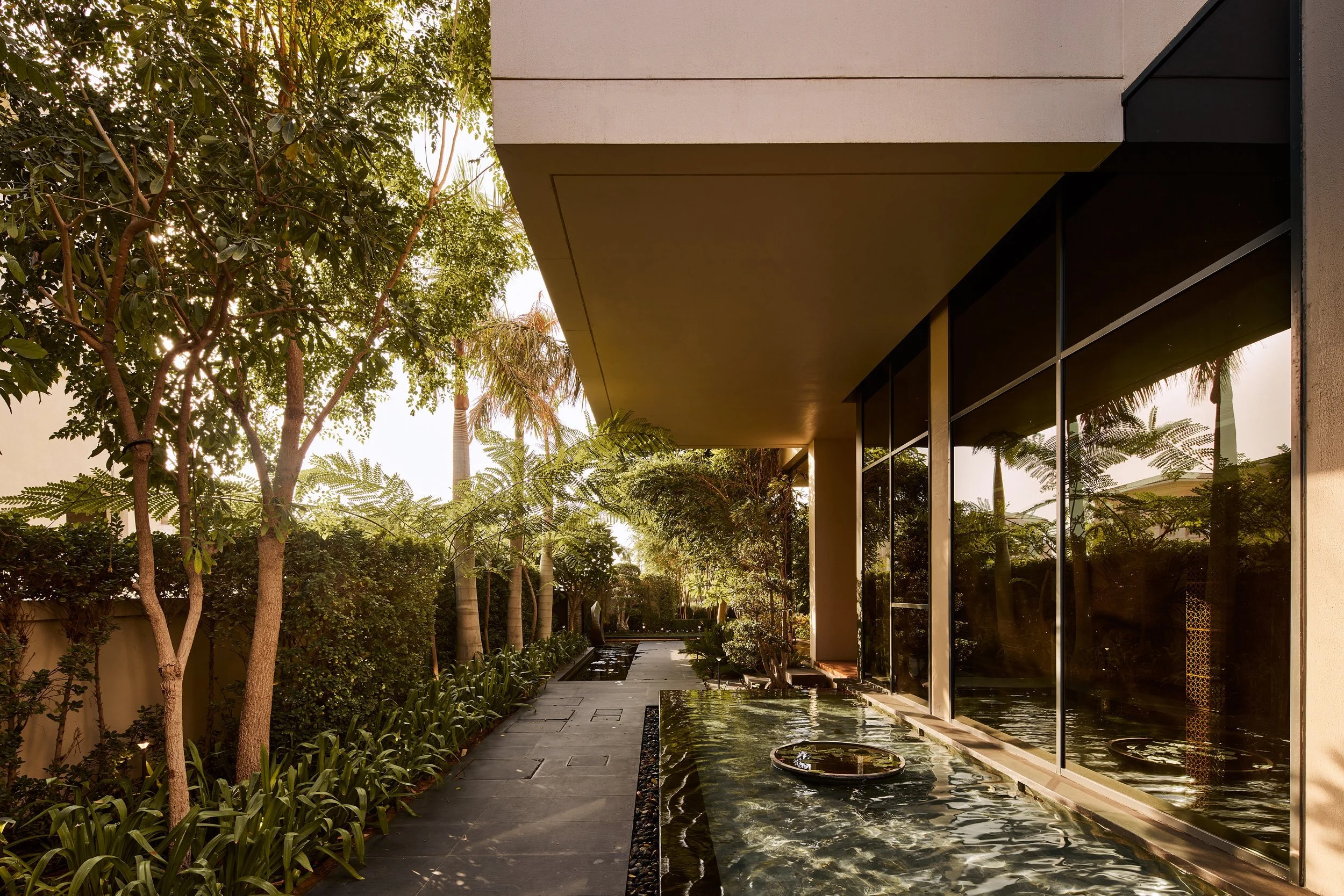 Garden path beside a water channel and a glass-walled wing of M Villa, Dubai Hills Estate