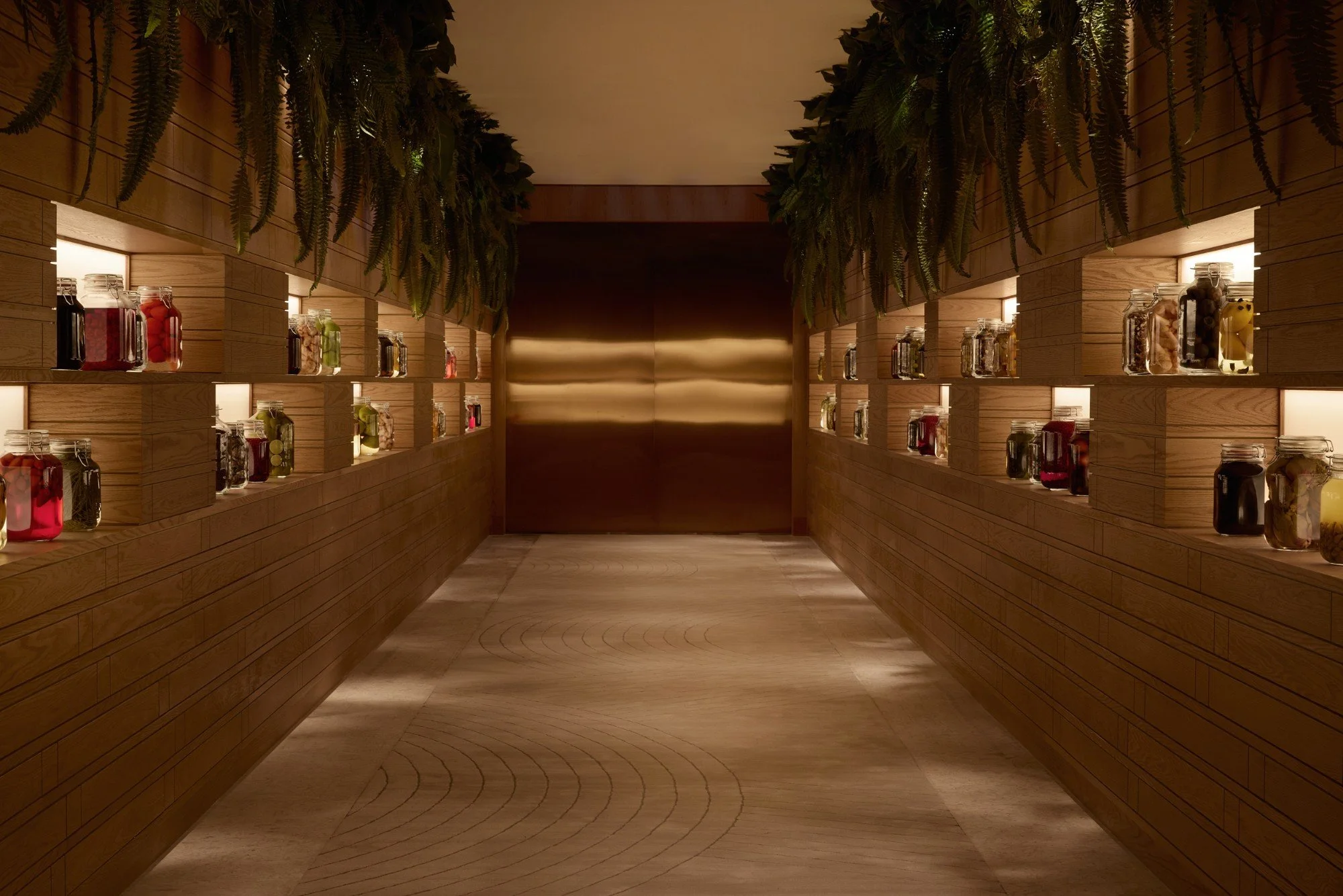Corridor at Restaurant Fzn lined with timber shelves of preserved jars beneath hanging ferns, Dubai