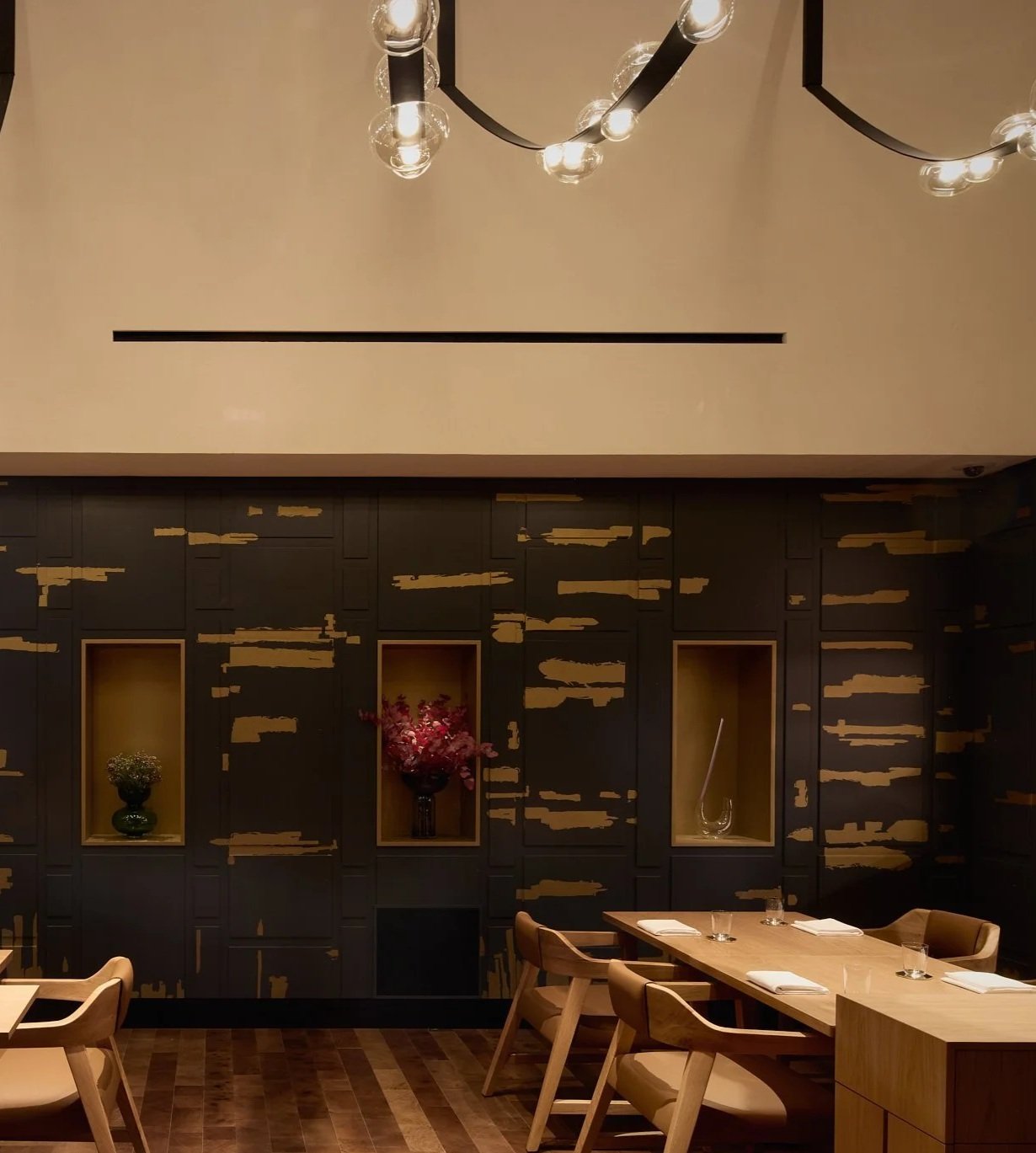 Dining room at Restaurant Fzn with pale timber tables and dark gilded wall panelling, Dubai