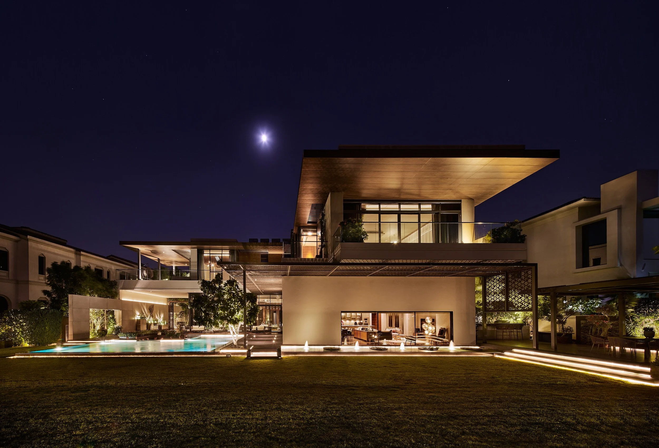Courtyard fountains lit at night between glass and stone wings of M Villa, Dubai Hills Estate