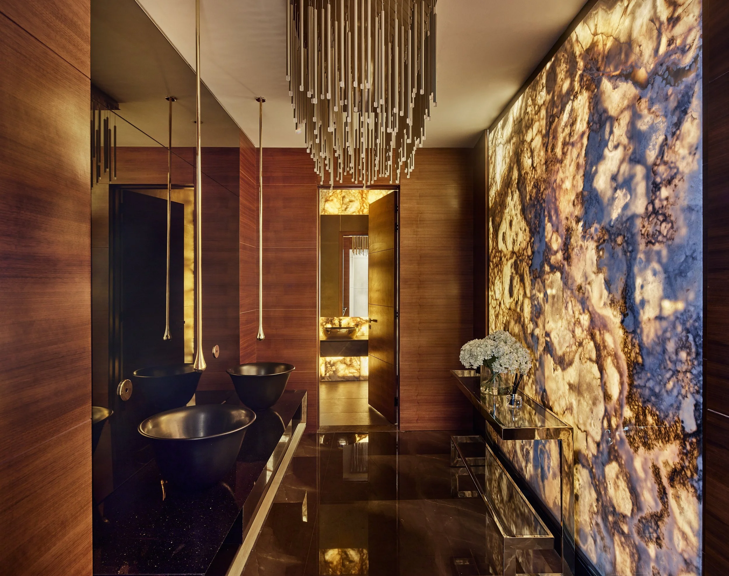 Powder room with a backlit onyx wall, black basins and a tall chandelier, M Villa, Dubai Hills Estate