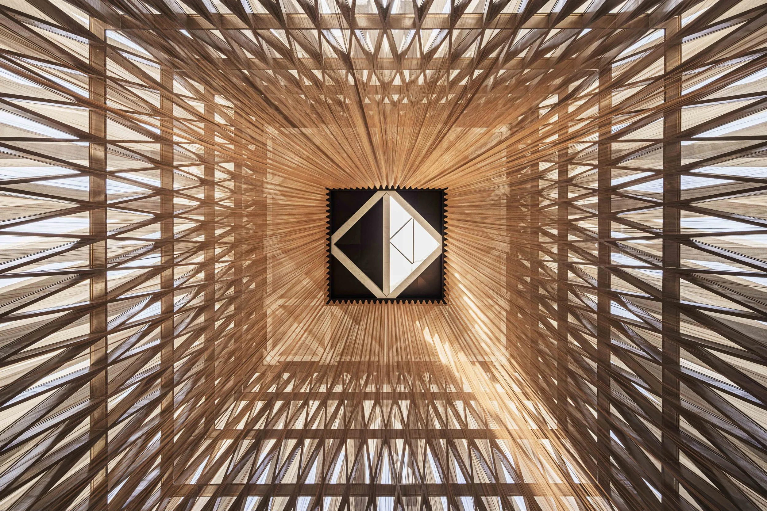 Looking up at the timber lattice ceiling and square skylight of the Moses Ben Maimon Synagogue, Abrahamic Family House, Abu Dhabi. Architect Adjaye Associates