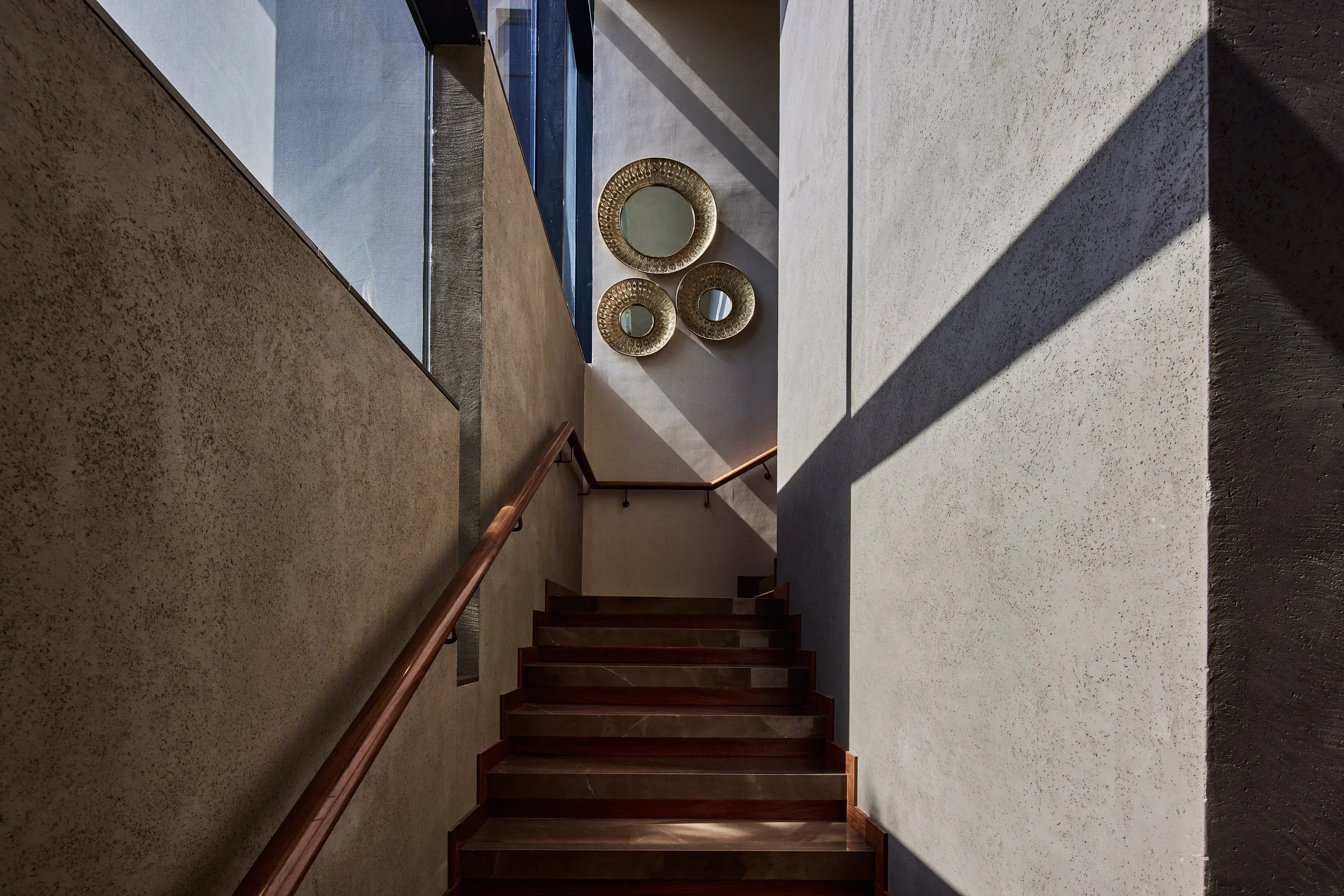 Staircase with a timber handrail between textured plaster walls, M Villa, Dubai Hills Estate