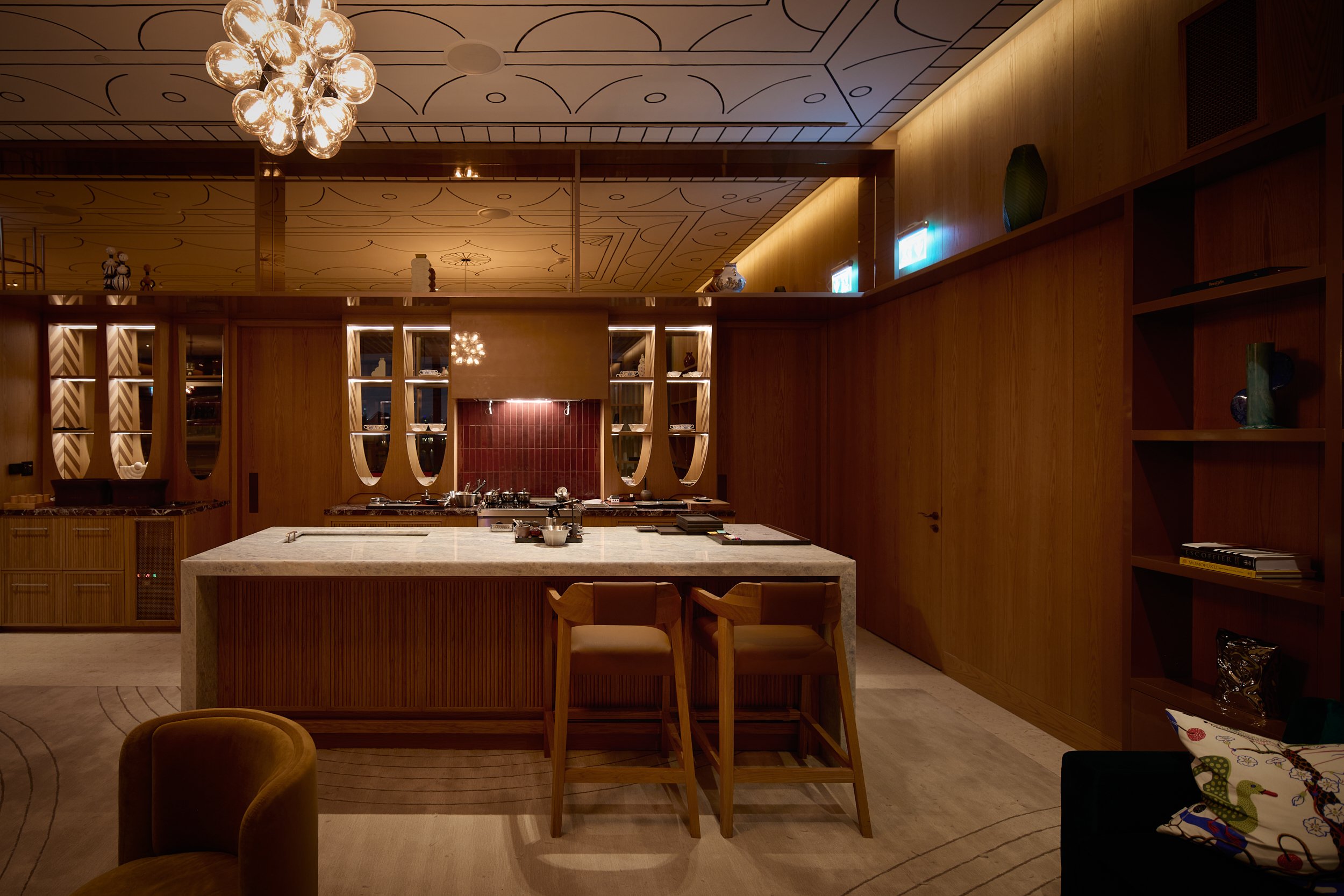 Open kitchen island with a marble counter and leather bar stools in front of a red-tiled kitchen at Restaurant Fzn, Dubai