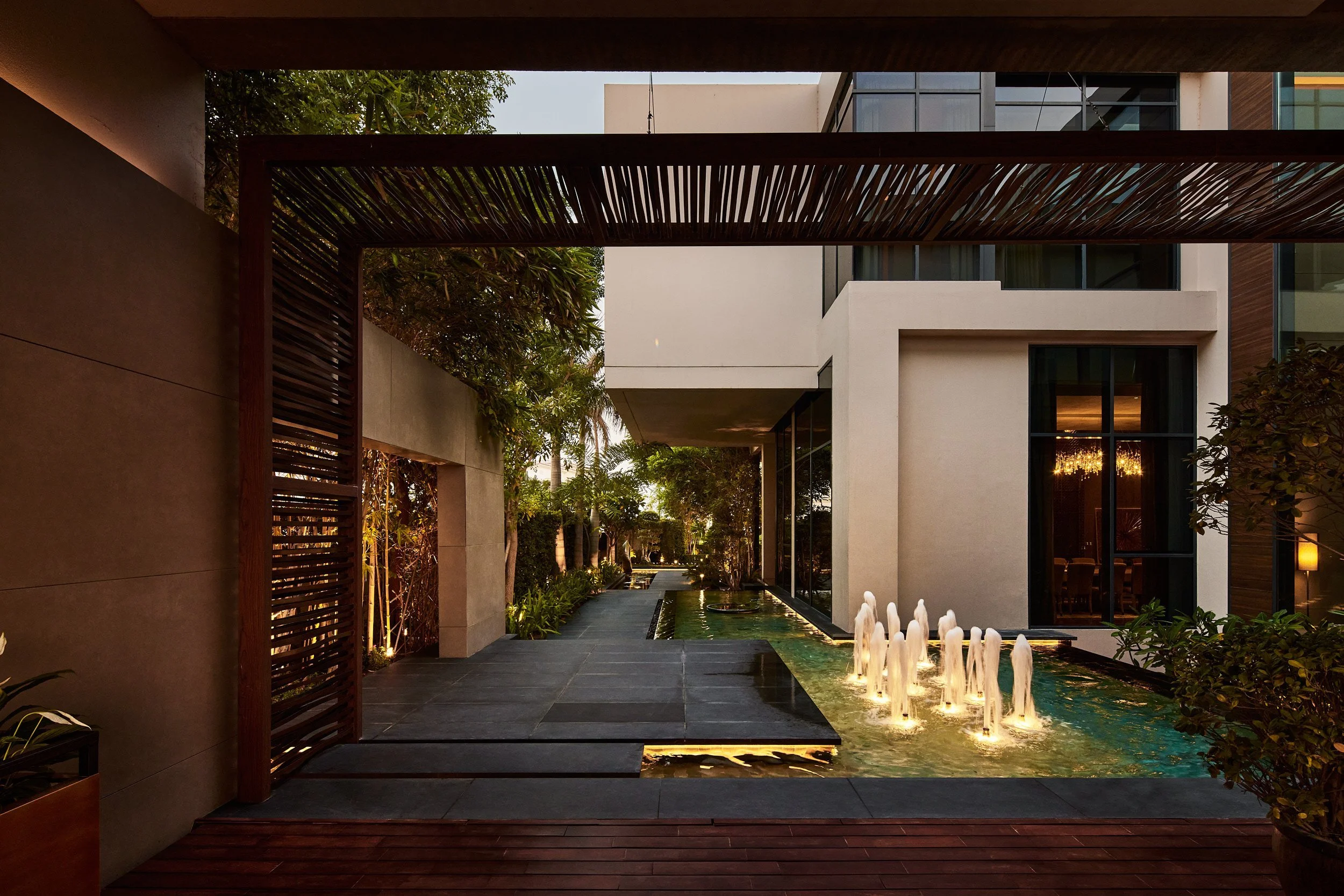 Entrance walkway beside lit fountains and a timber pergola at dusk, M Villa, Dubai Hills Estate