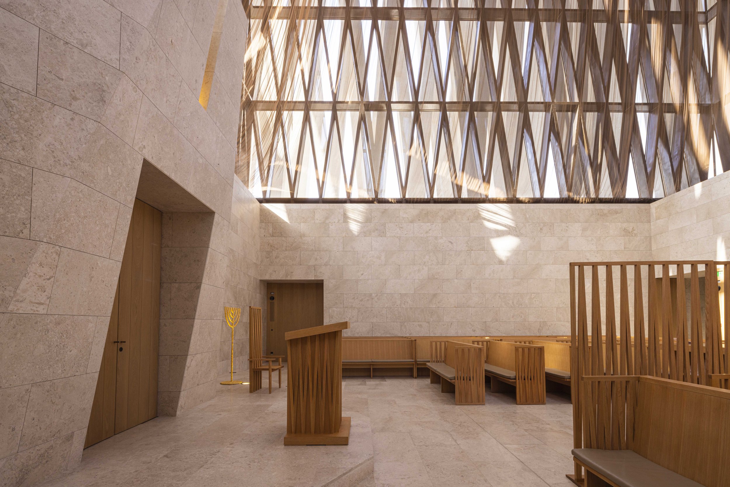 Timber lattice roof, limestone walls and wooden benches inside the Moses Ben Maimon Synagogue, Abrahamic Family House, Abu Dhabi. Architect Adjaye Associates