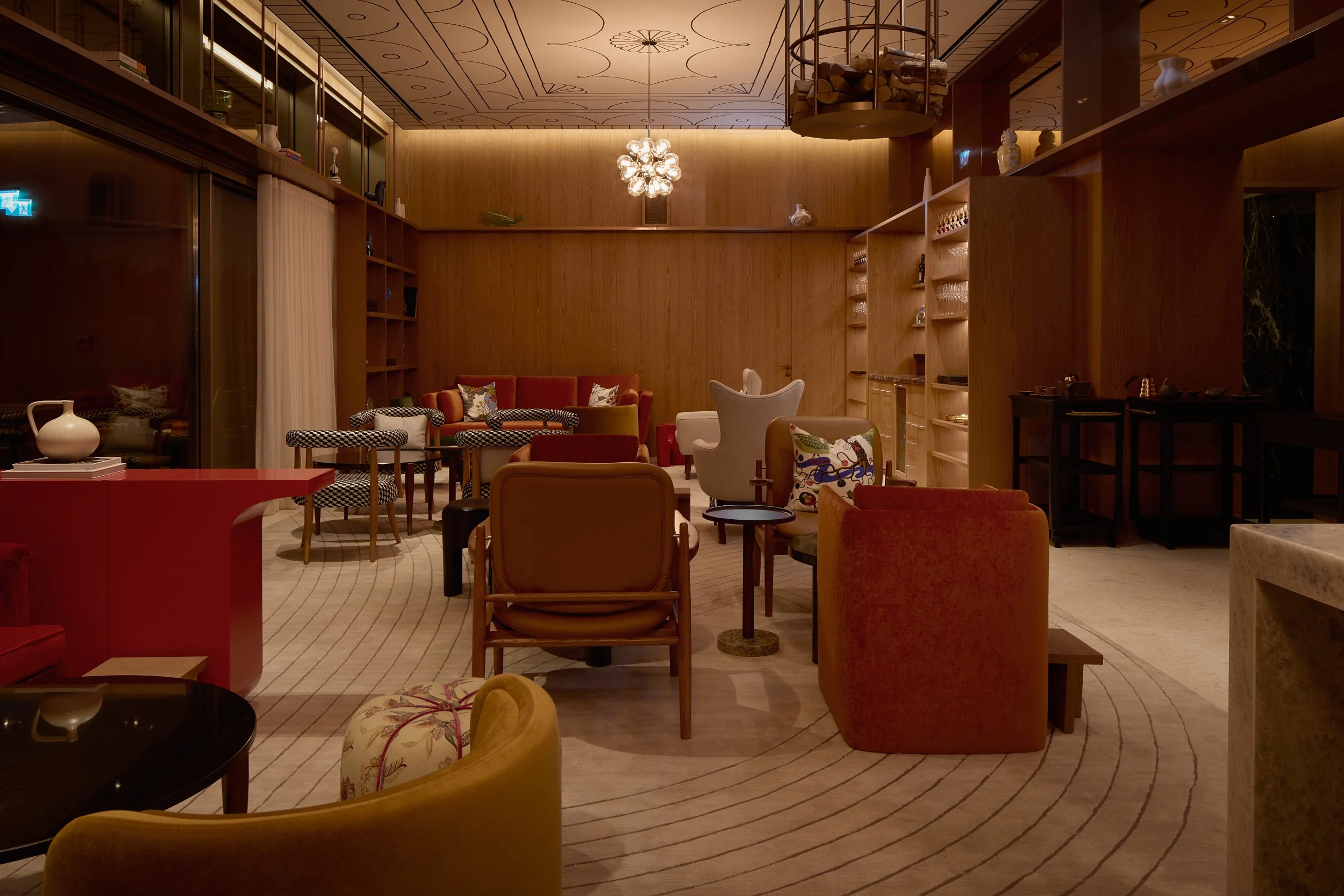 Upstairs lounge at Restaurant Fzn with timber-panelled walls, red and orange armchairs and a checkerboard-upholstered chair, Dubai