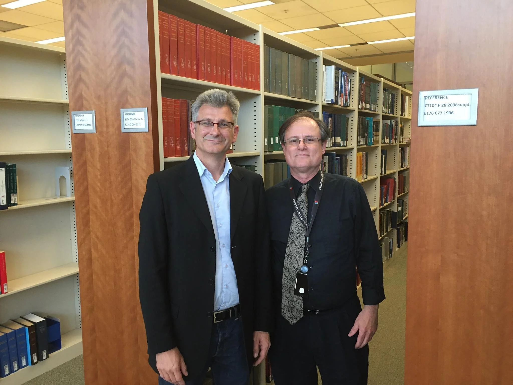 Two men standing in a library with bookshelves behind them.