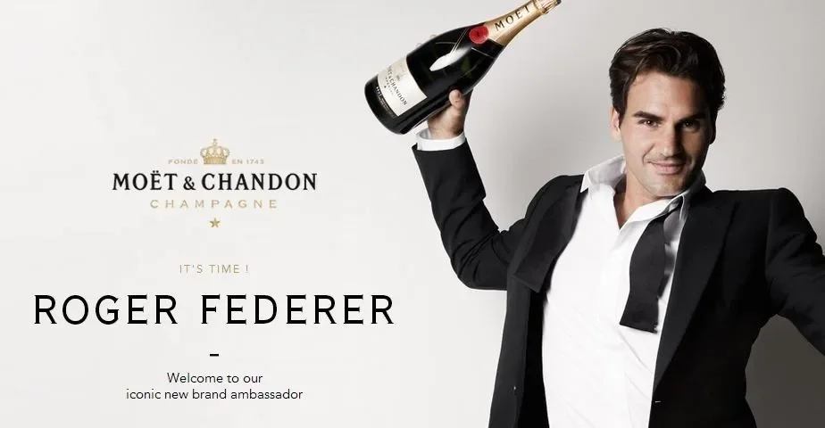 A man in a black suit and white shirt holding a bottle of Moët & Chandon champagne over his shoulder, smiling, with text announcing Roger Federer as the new brand ambassador for Moët & Chandon.