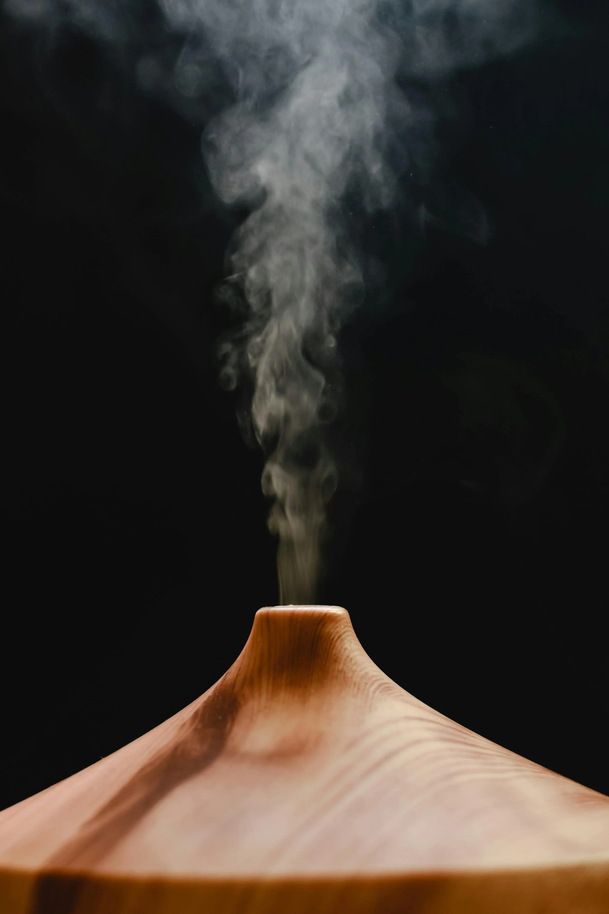 A wooden diffuser emitting vapor against a black background.