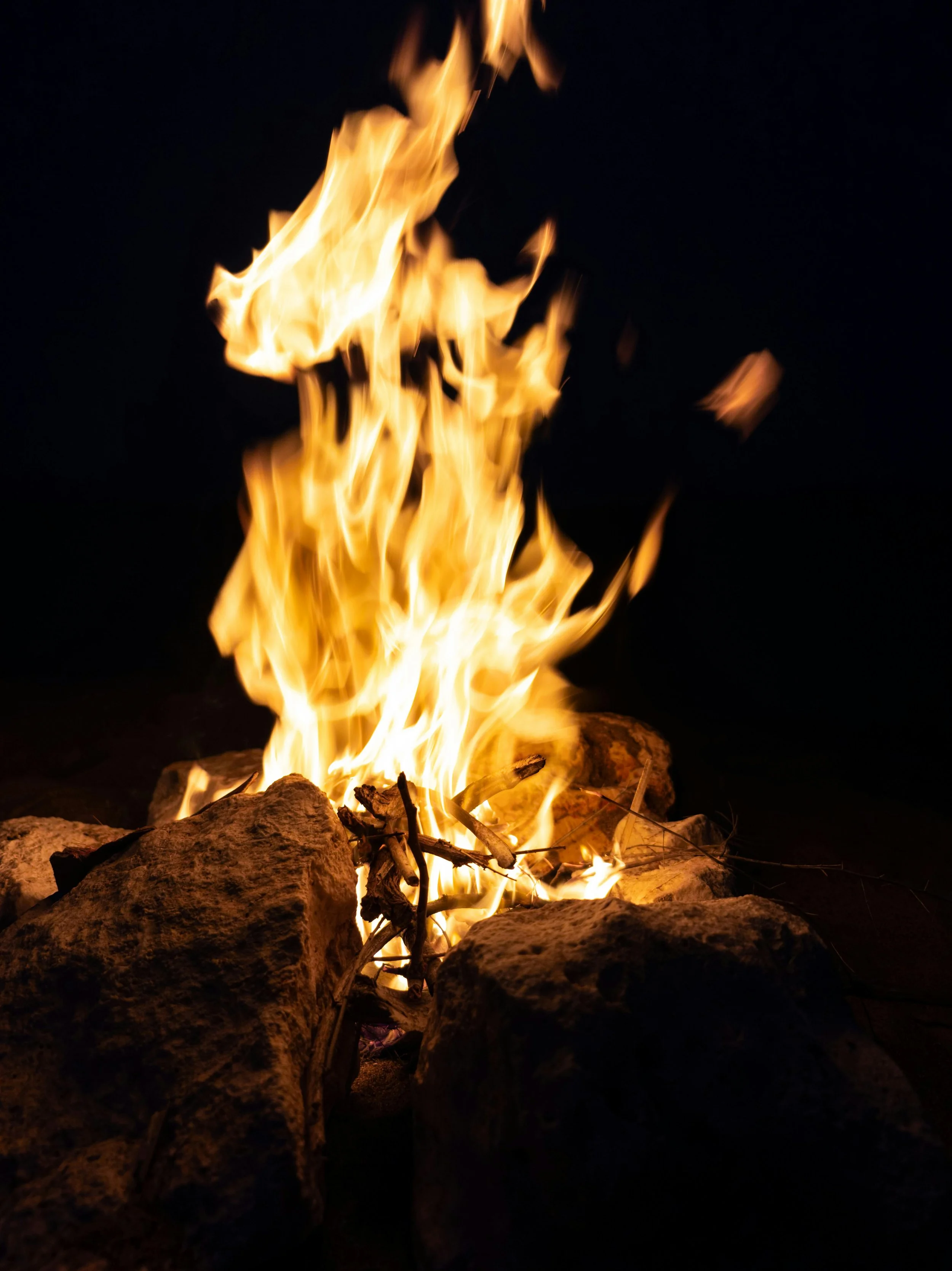 Fire burning among rocks at night with dark background.