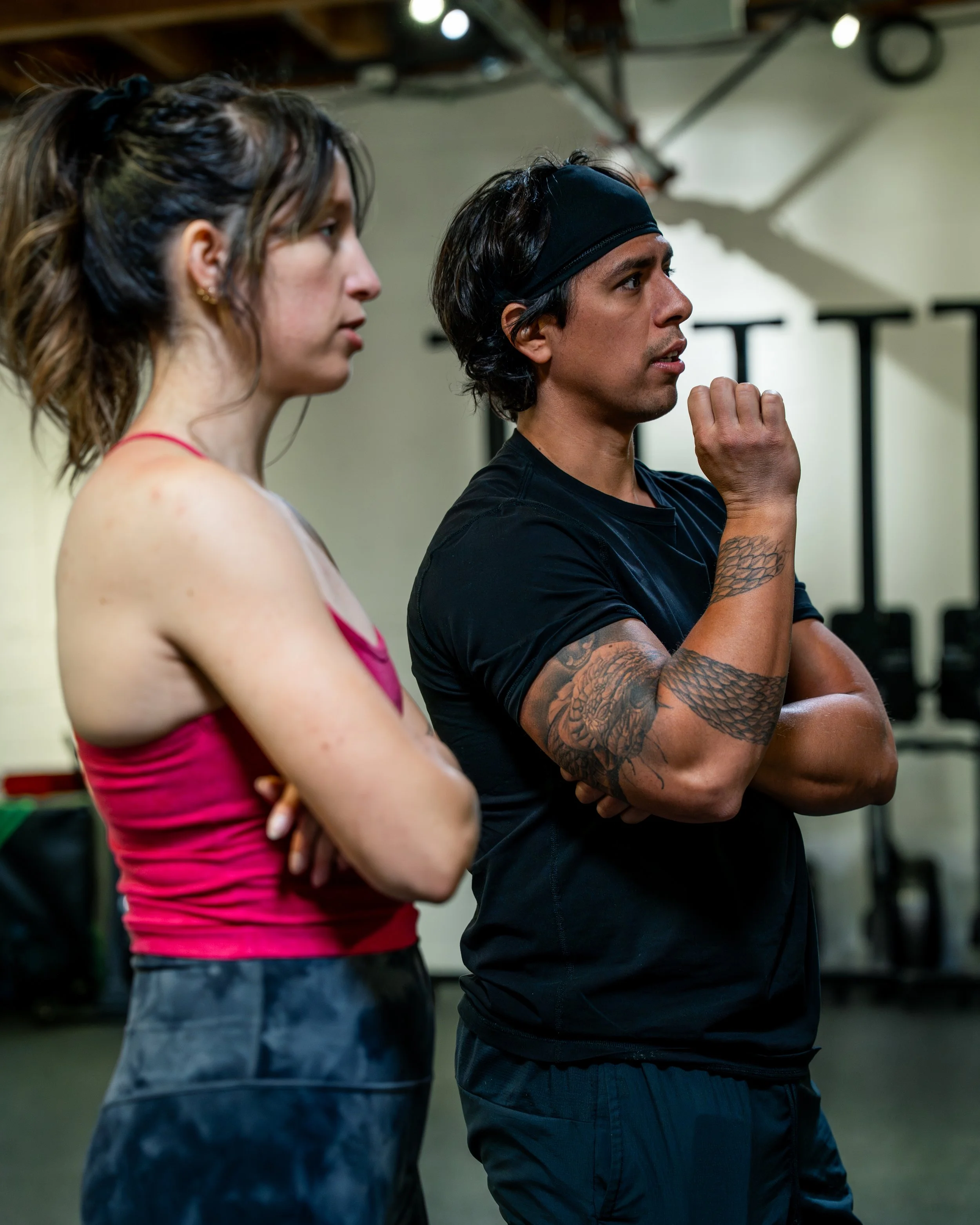 Two women next to a wall; one holding a weight plate, the other wearing a gray shirt.