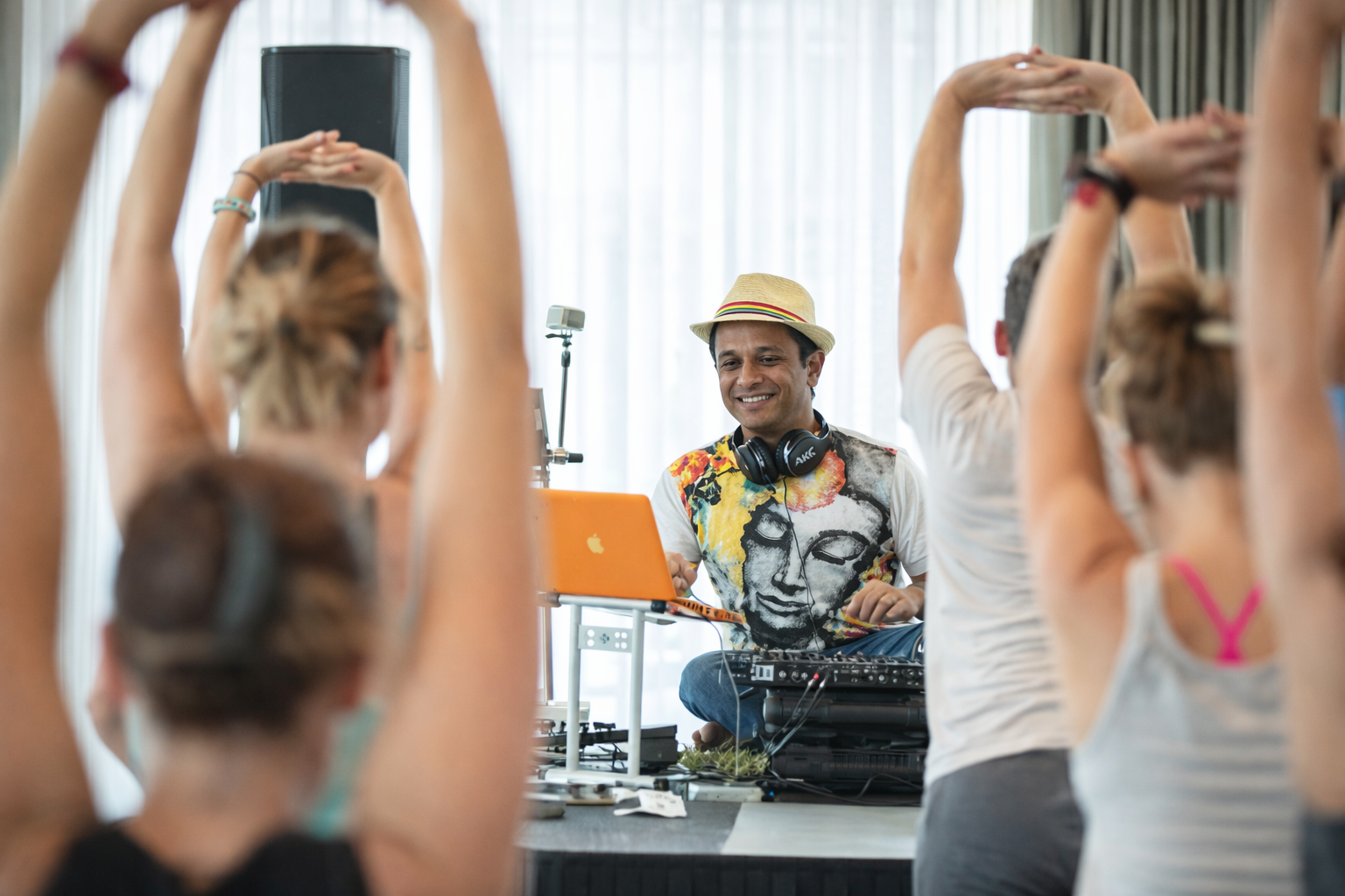 A man leading a yoga or dance class with several women stretching with arms overhead in a bright room.