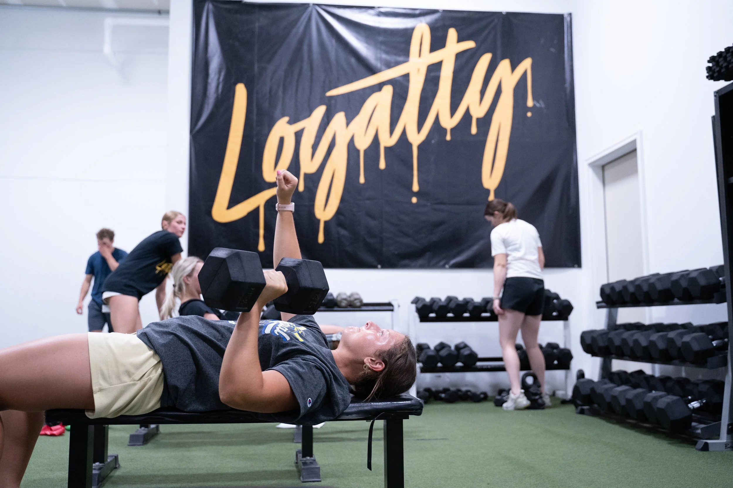 Athlete doing a dumbbell bench press in front of the gold Loyalty banner