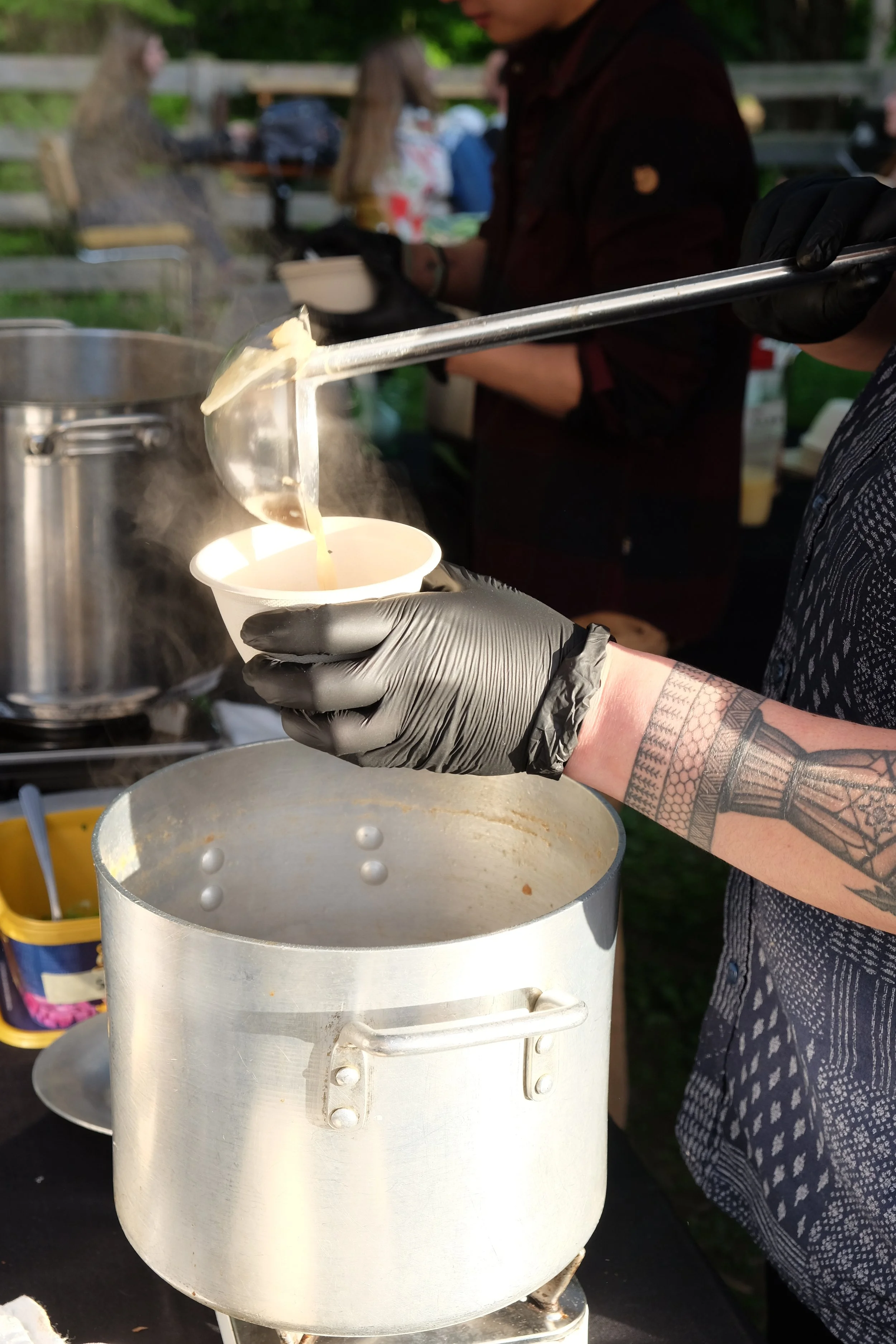 Tatooed person ladling soup from a big pot