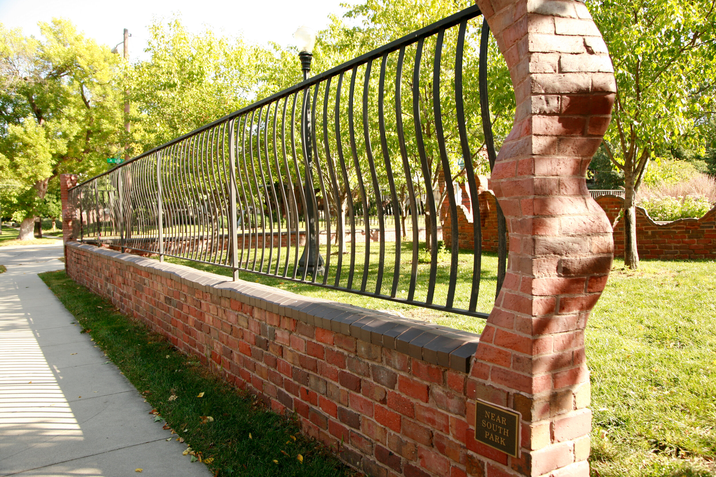 Carved red brick column with iron fence creates a sculptural edge to city park in Lincoln, NE