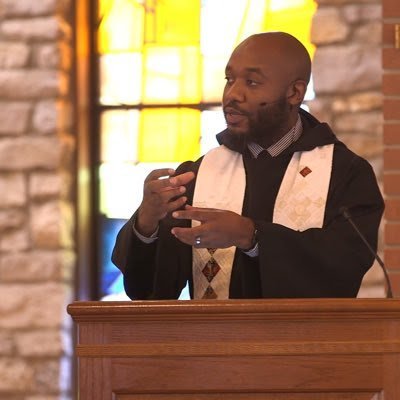 Meshach Kanyion preaching from a wooden pulpit inside a church.