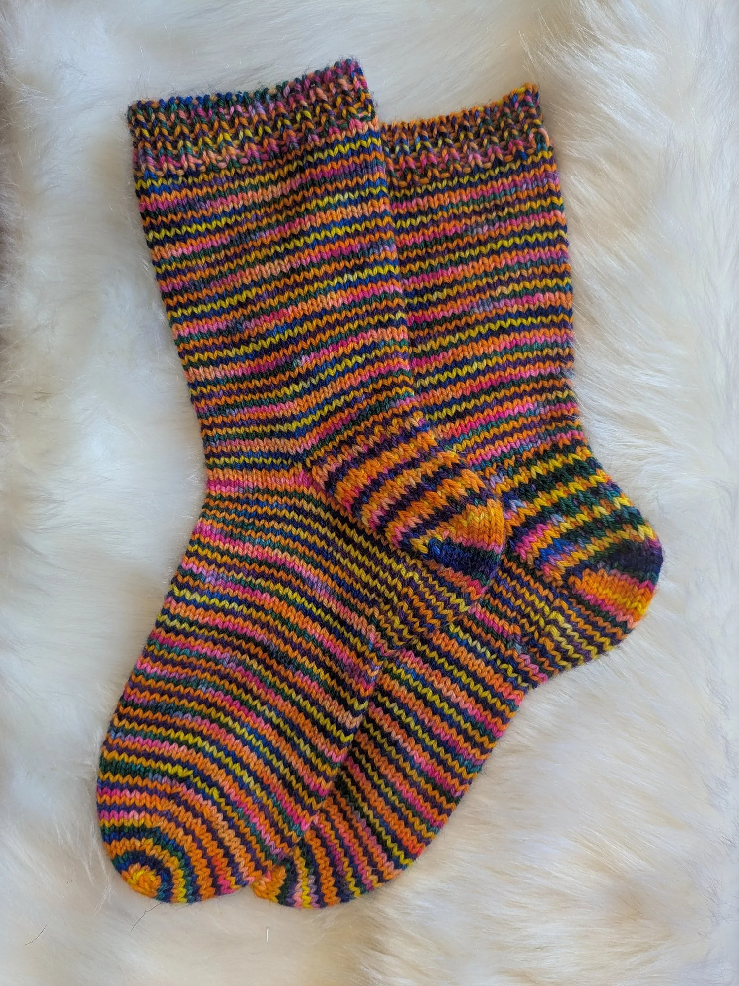 Two colourfully striped socks are laid flat on a soft, off-white background.