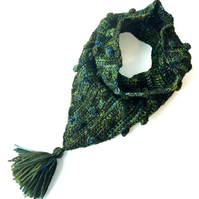 A bandana-style cowl with a large tassel lays flat on a white background.