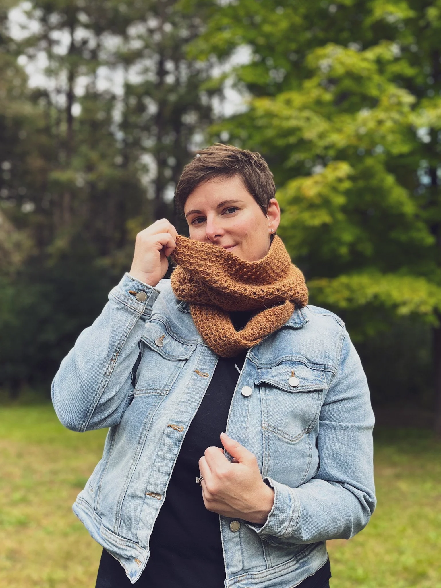A woman with short hair is wearing a light coloured denim jacket with a rust coloured infinity scarf.