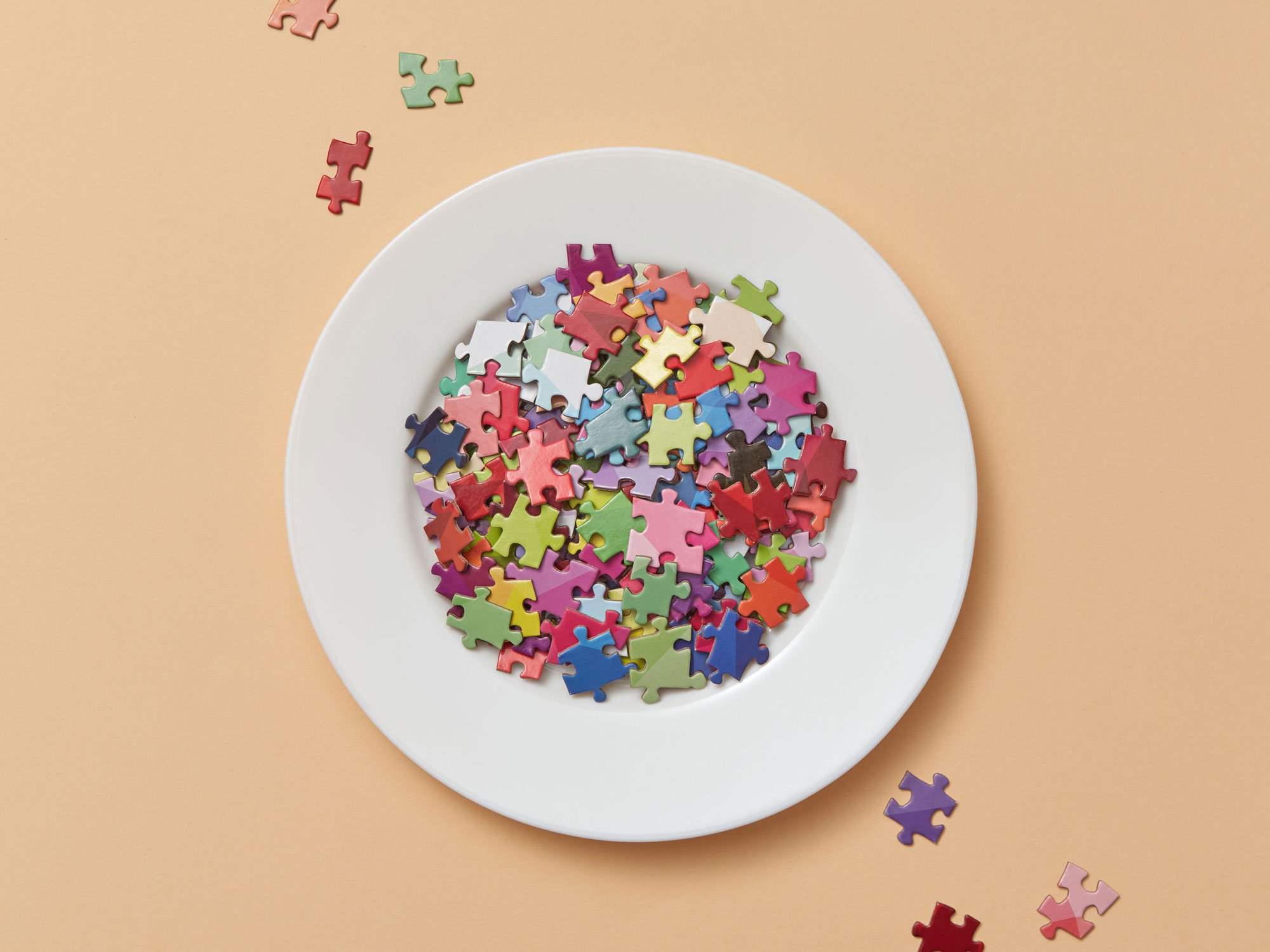 A white plate holding a small pile of colourful jigsaw pieces