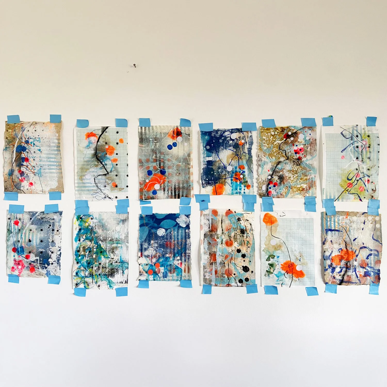 Twelve pages of abstract sketchbook work taped in two rows on a white studio wall