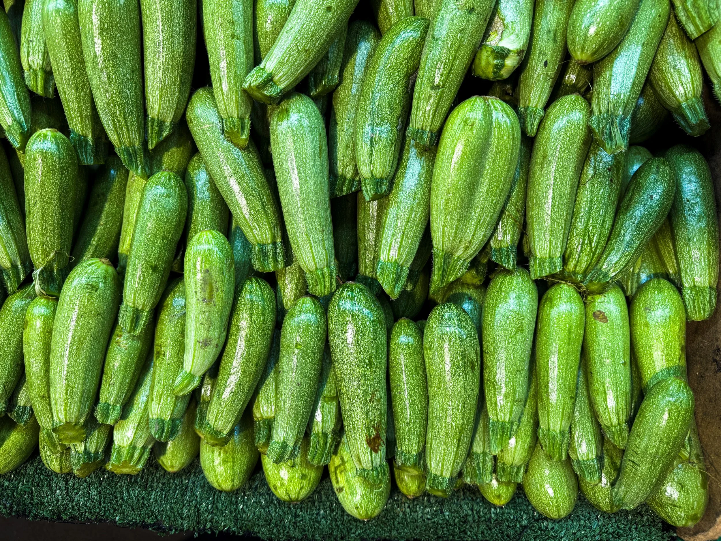 Dozens of pale green courgettes packed in tight rows in a crate, filling the frame