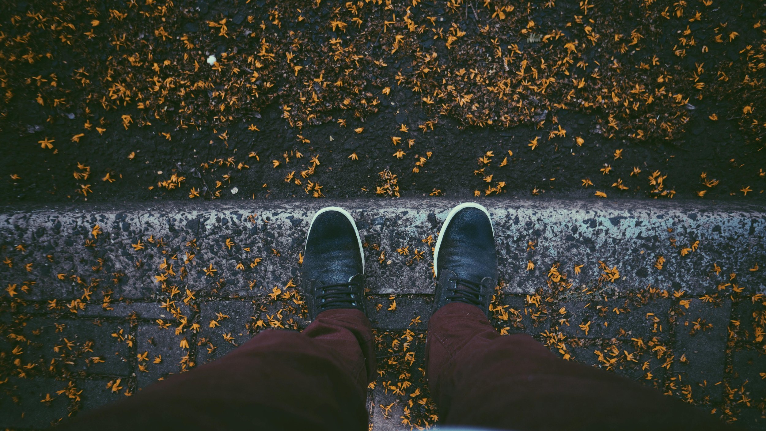 Feet on the edge of a pavement scattered with Autumn leaves