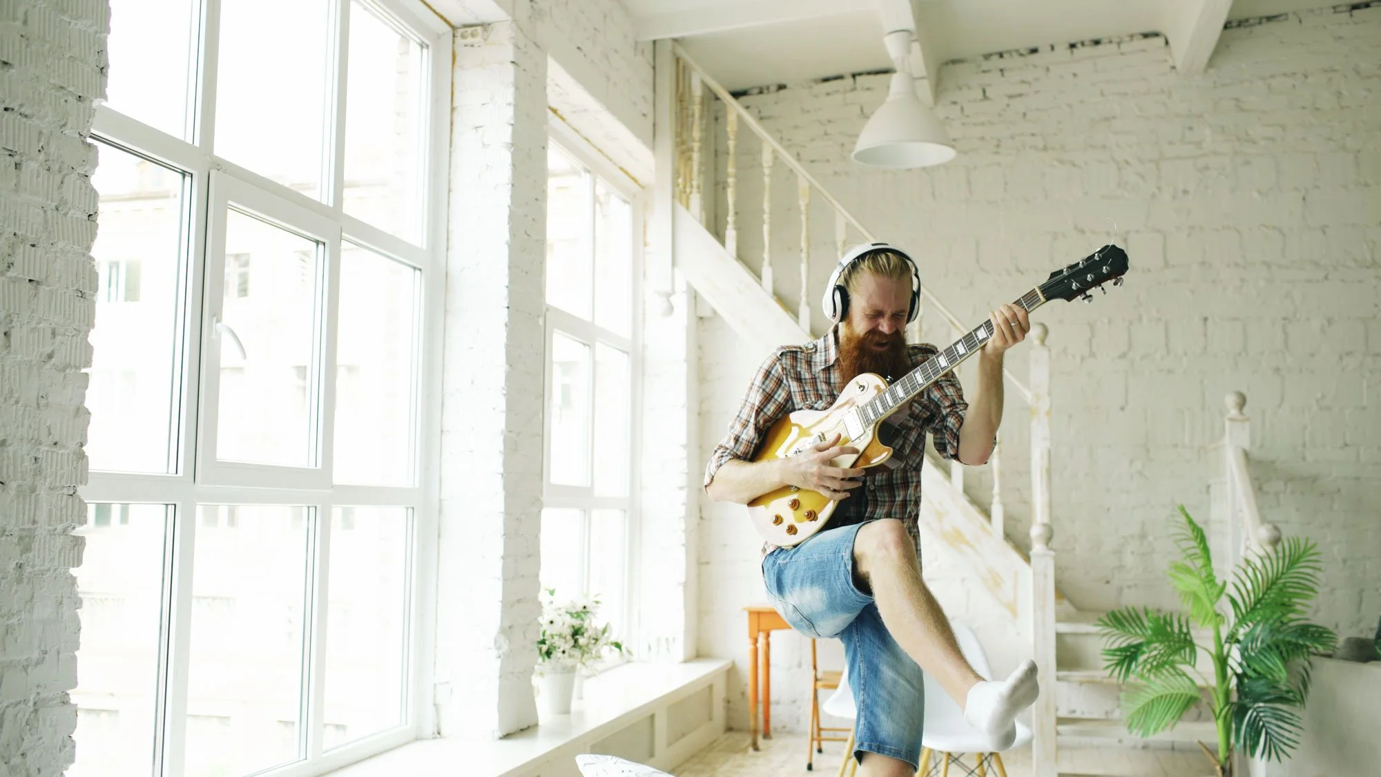 A man playing electric guitar in a bright loft room