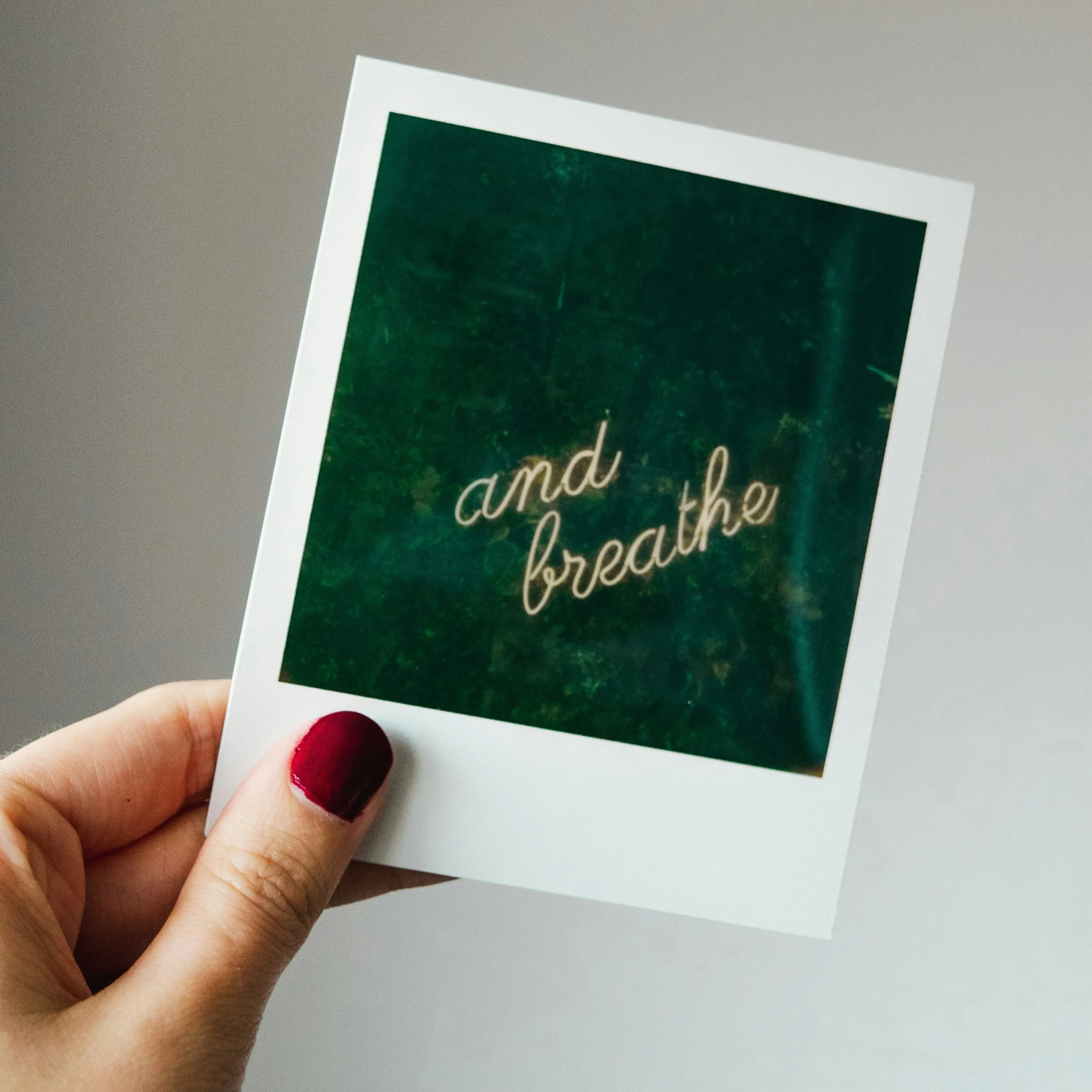 Hand holding a polaroid photo saying 'and breath' in neon