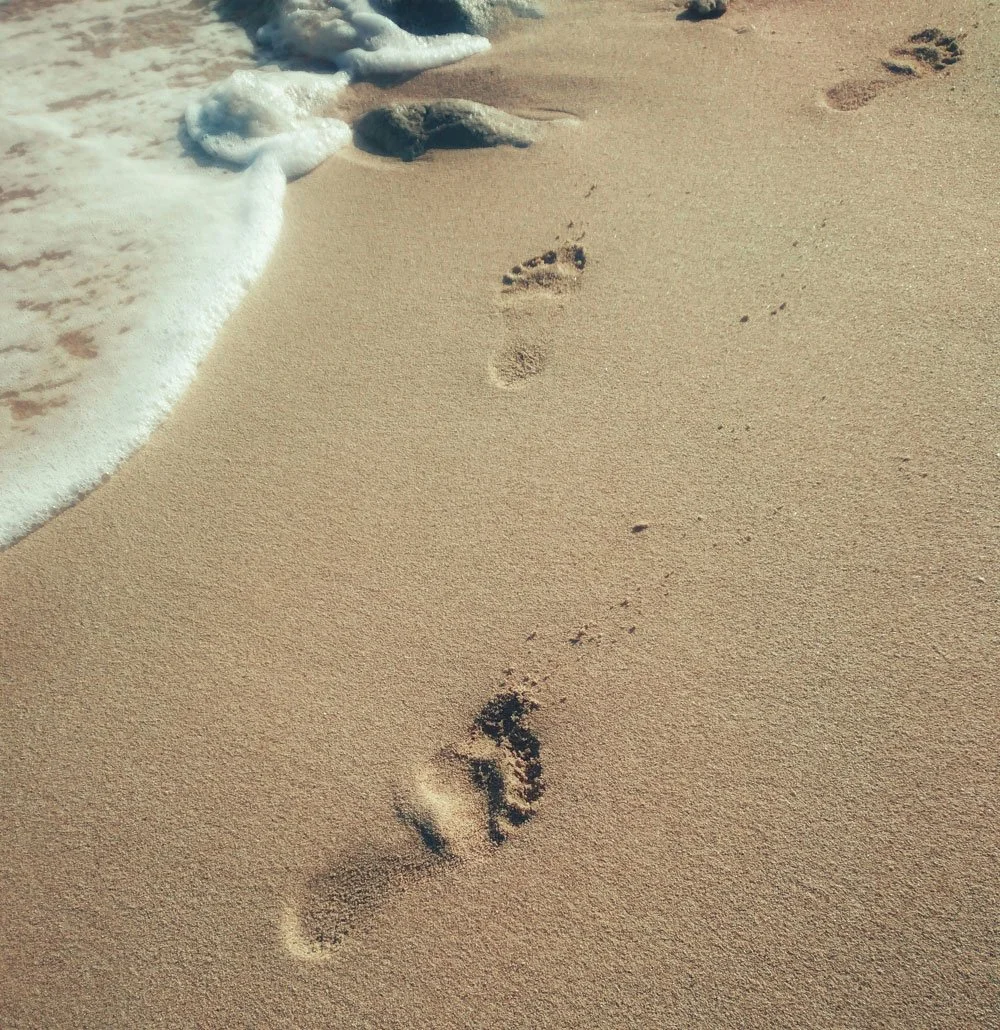 Footprints in sand along the water's edge with waves washing over them
