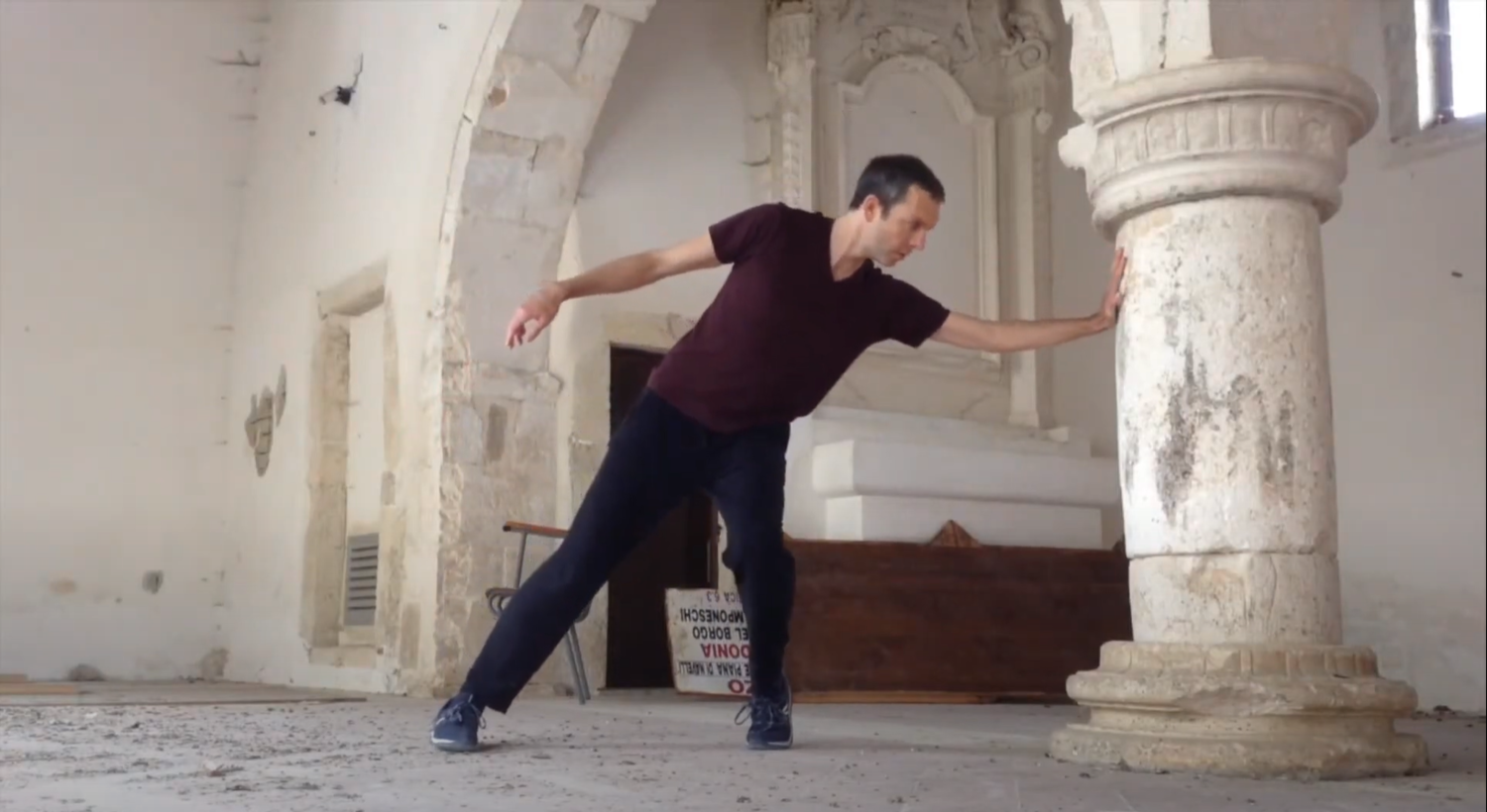Kevin Skelton dancing in one of the restored churches in Capestrano post-earthquake.Alt text: A man dances in front of an archway, gracefully extending an arm to touch a column as the rest of his body adjusts to the distance
