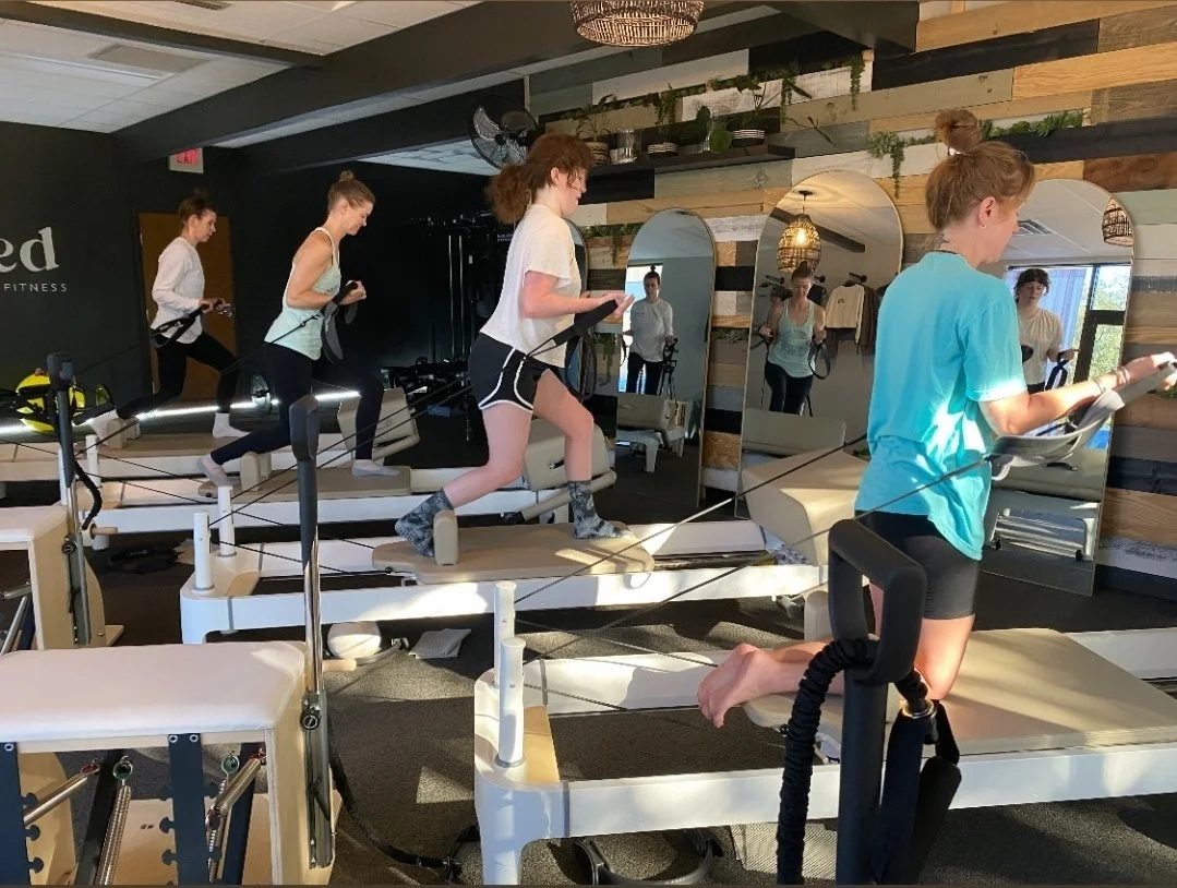 Women doing a lunge holding straps on a pilates reformer machine.