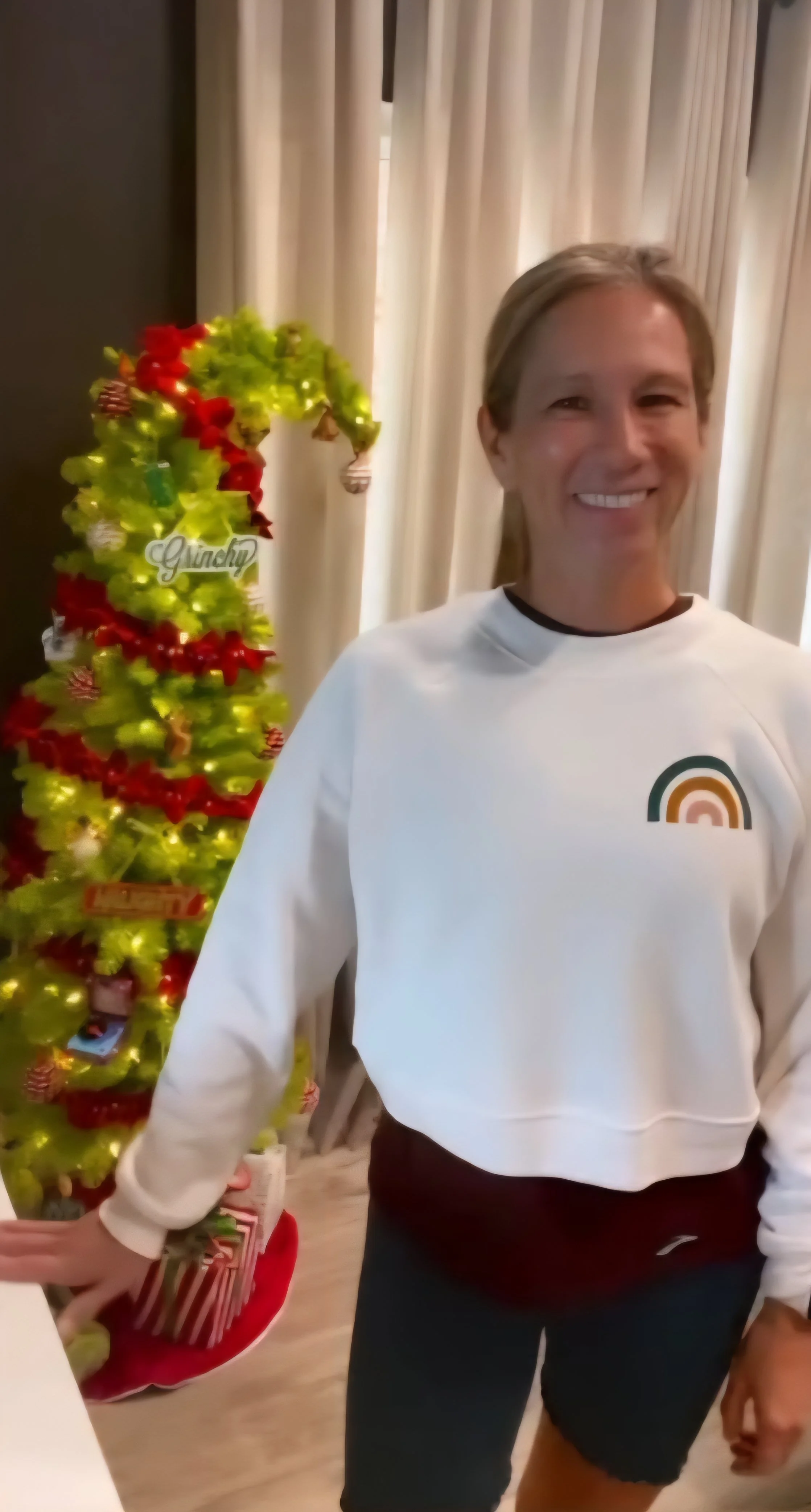 Woman posing by a Christmas tree, wearing a white cozy vintage pullover from Shed Pilates and Fitness.