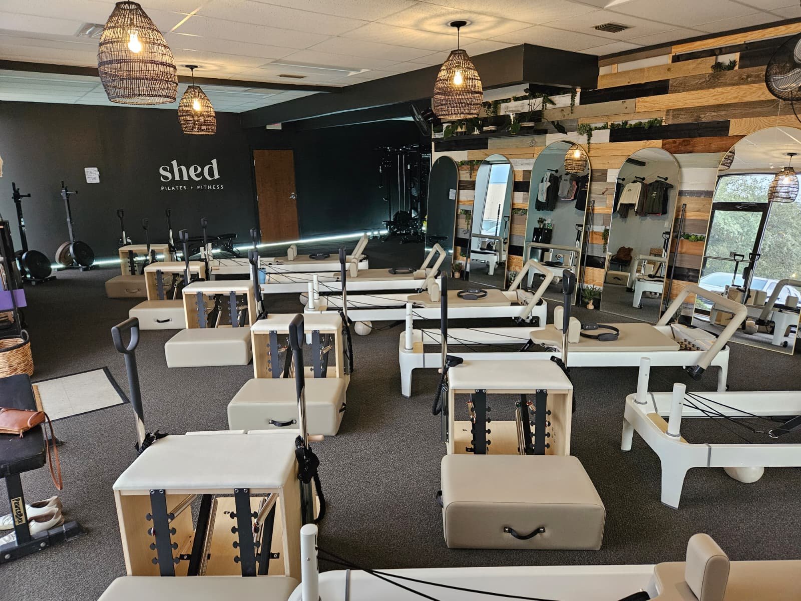 Interior of a Pilates and fitness studio with Pilates chairs, reformer machines, mirrors, and decorative lighting.