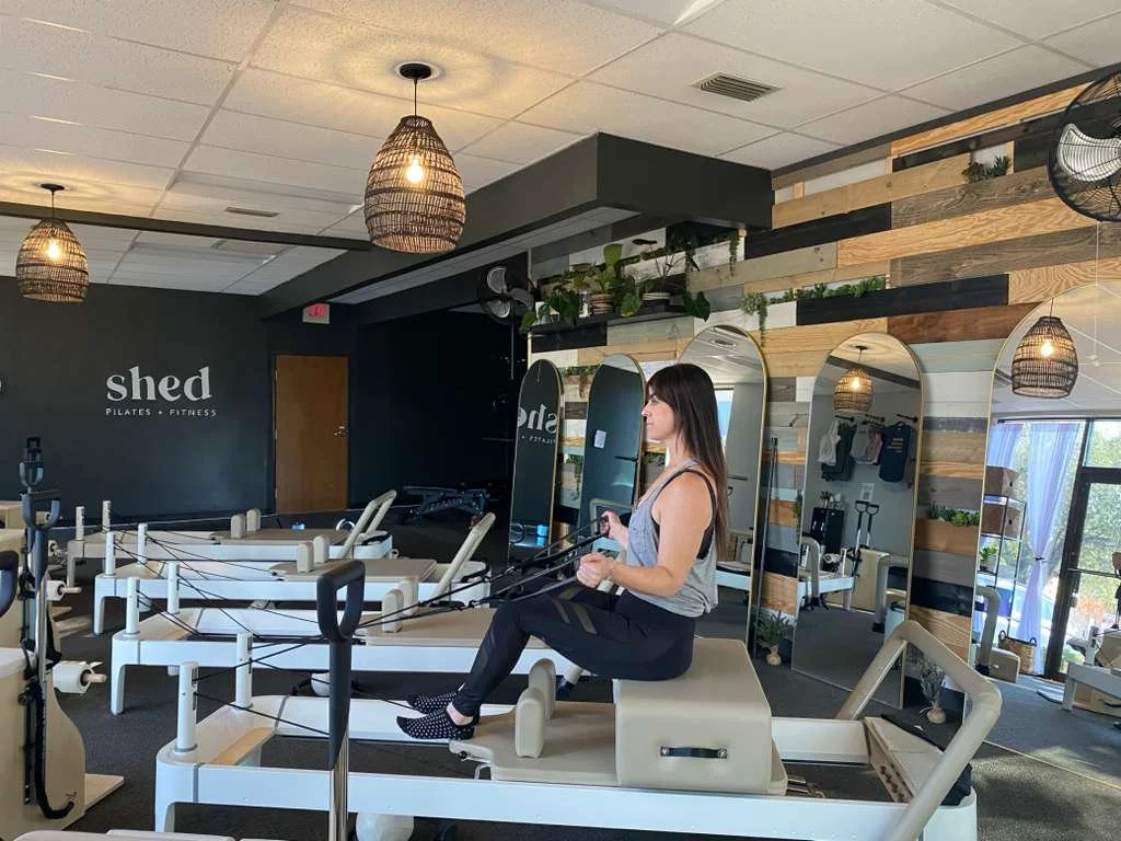 A woman at a Pilates studio using a reformer machine for exercise.