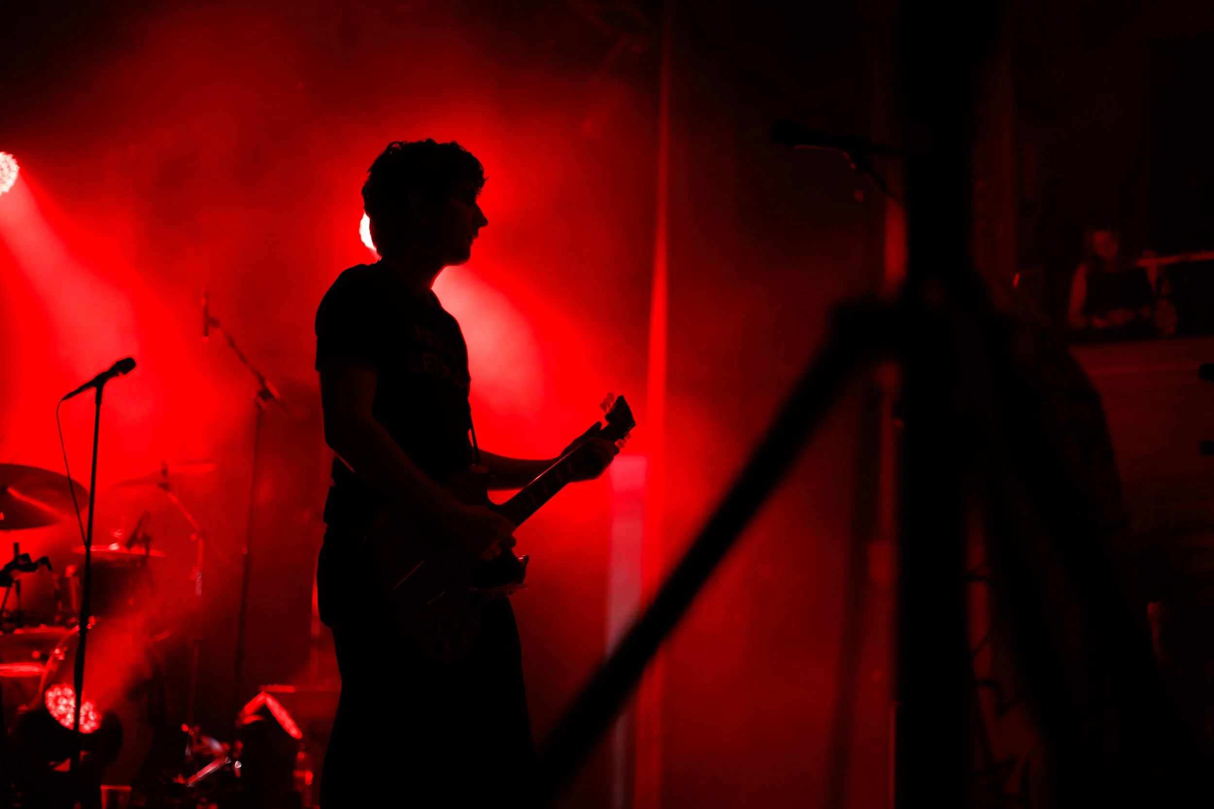 Silhouetted guitarist performing on stage under dramatic red lighting.