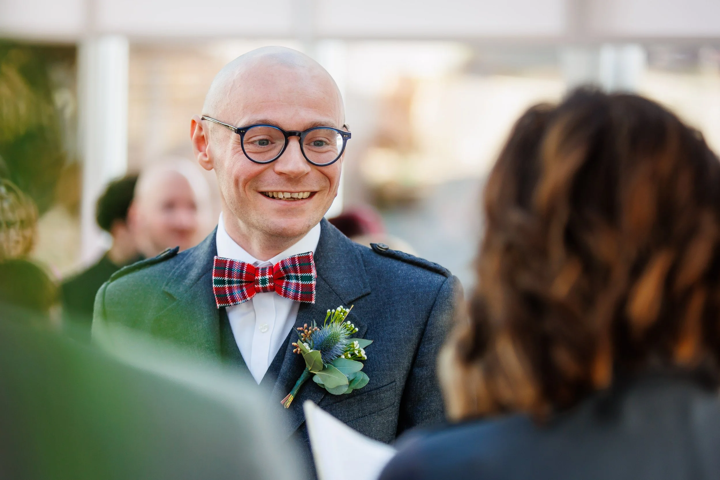 Groom in a tartan bow tie smiling during ceremony.