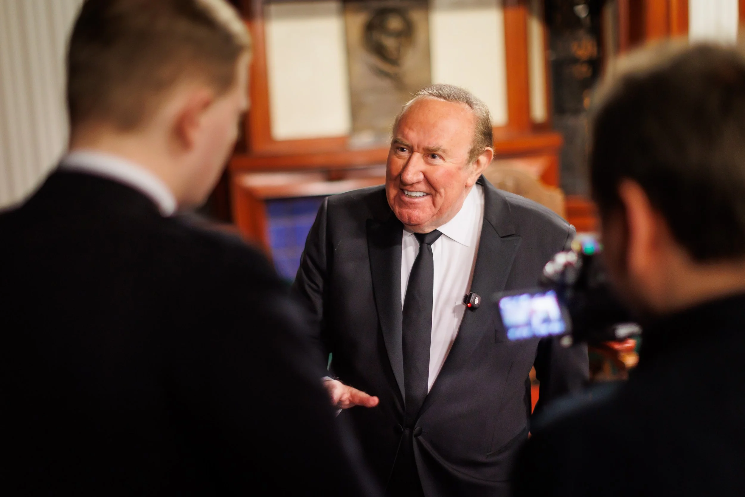 Andrew Neil in a suit speaking during an event, filmed by a small camera crew.