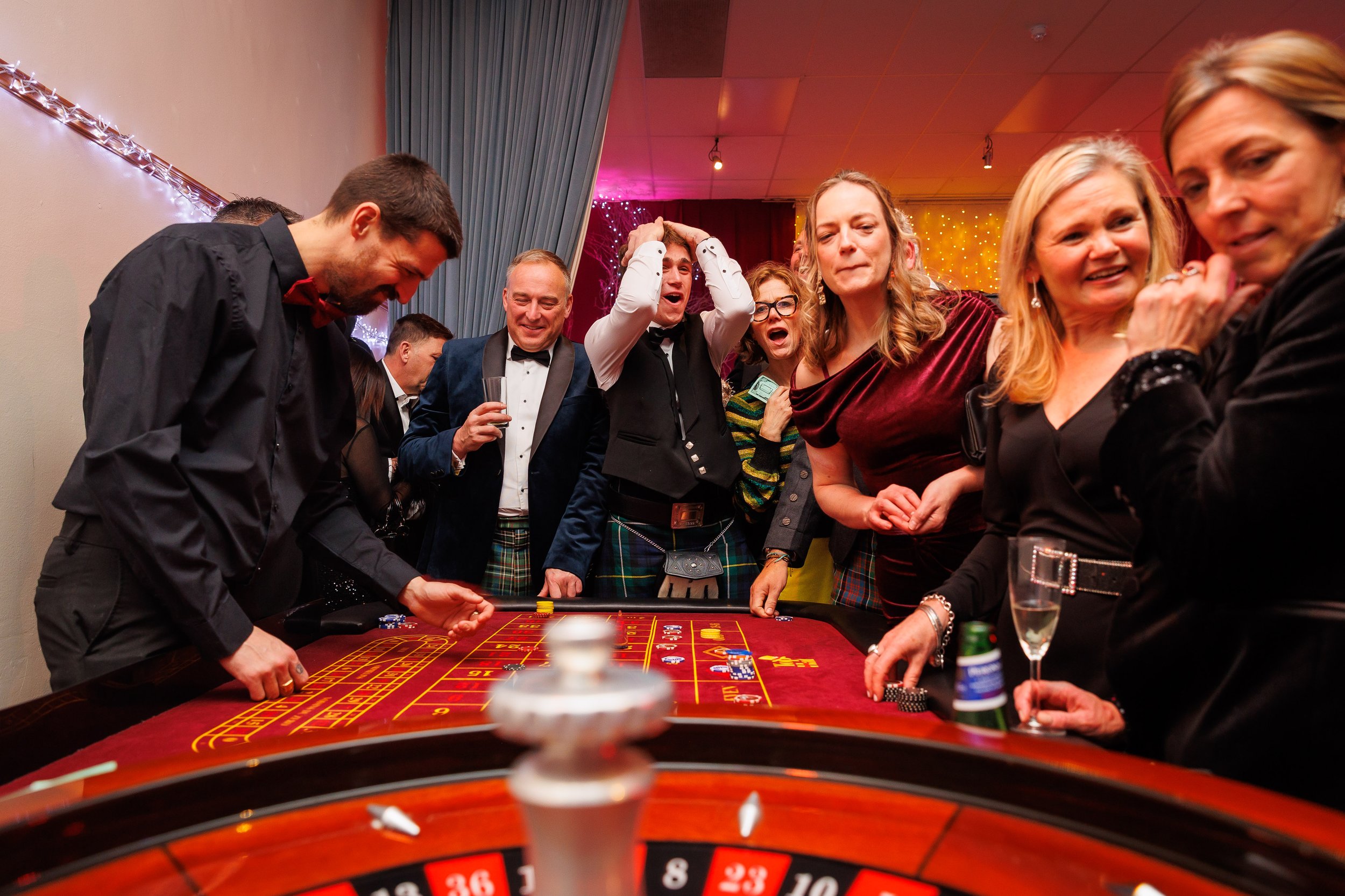Guests gathered around a roulette table at an evening event, reacting as the ball spins.