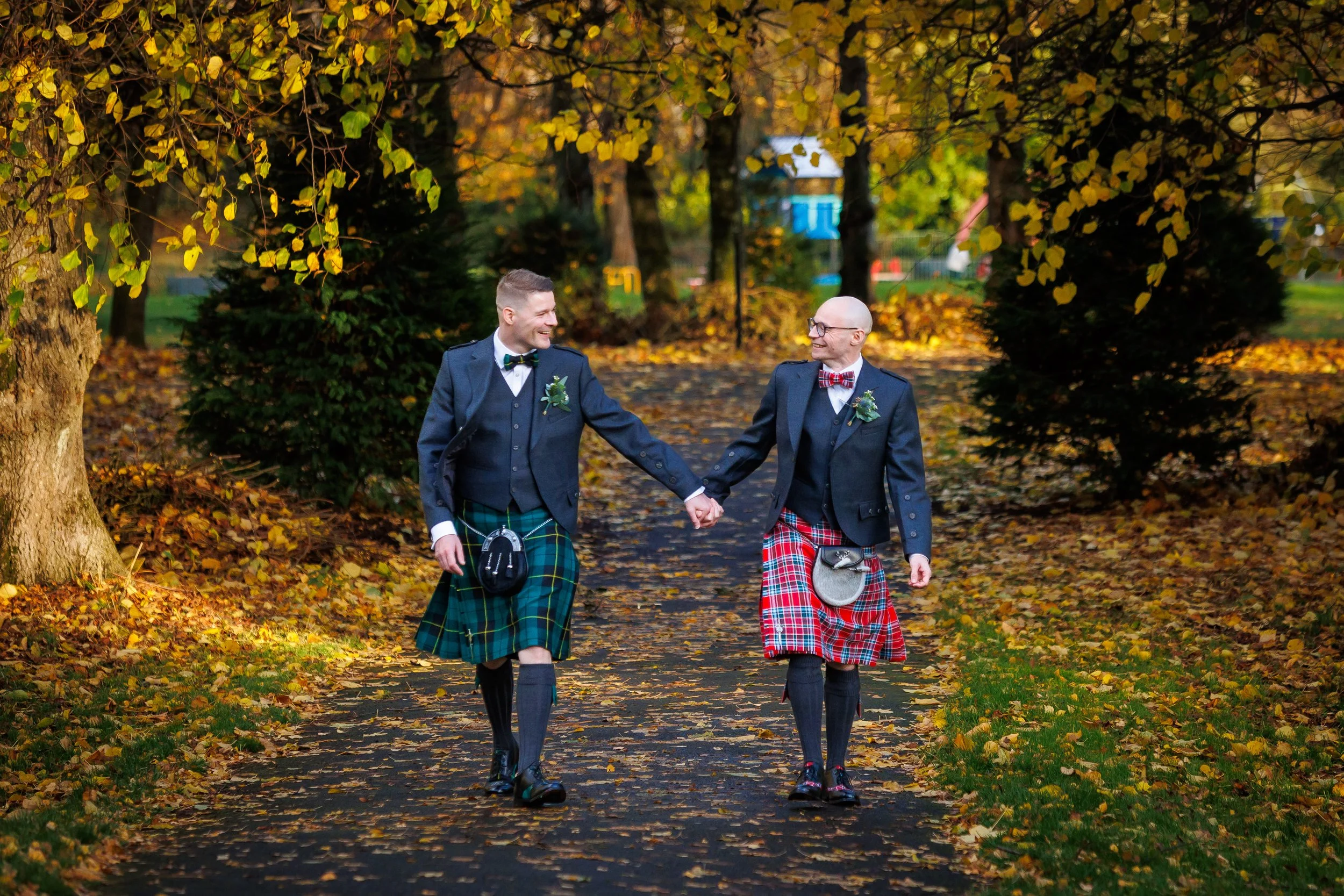 Two grooms holding hands and walking through Maxwell Park in autumn.