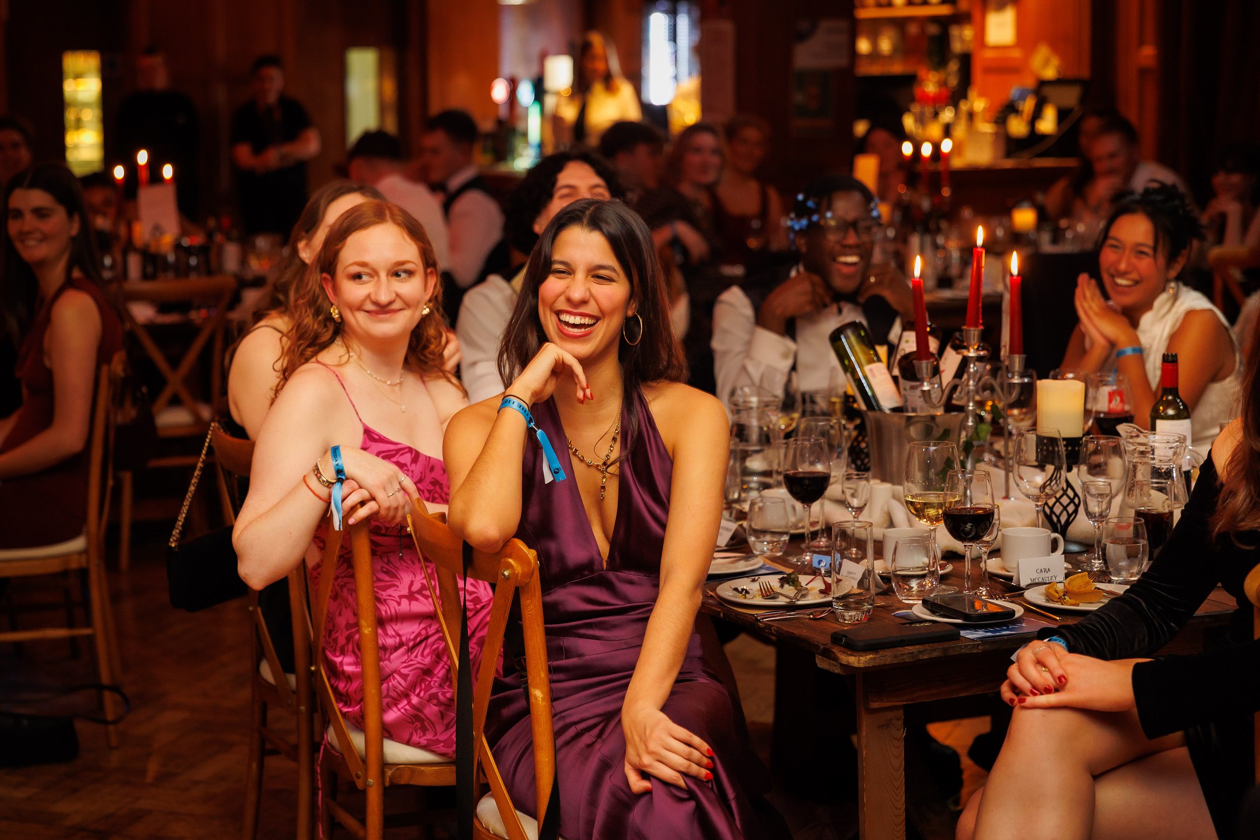 Guests laughing at a formal dinner event with candlelit tables.