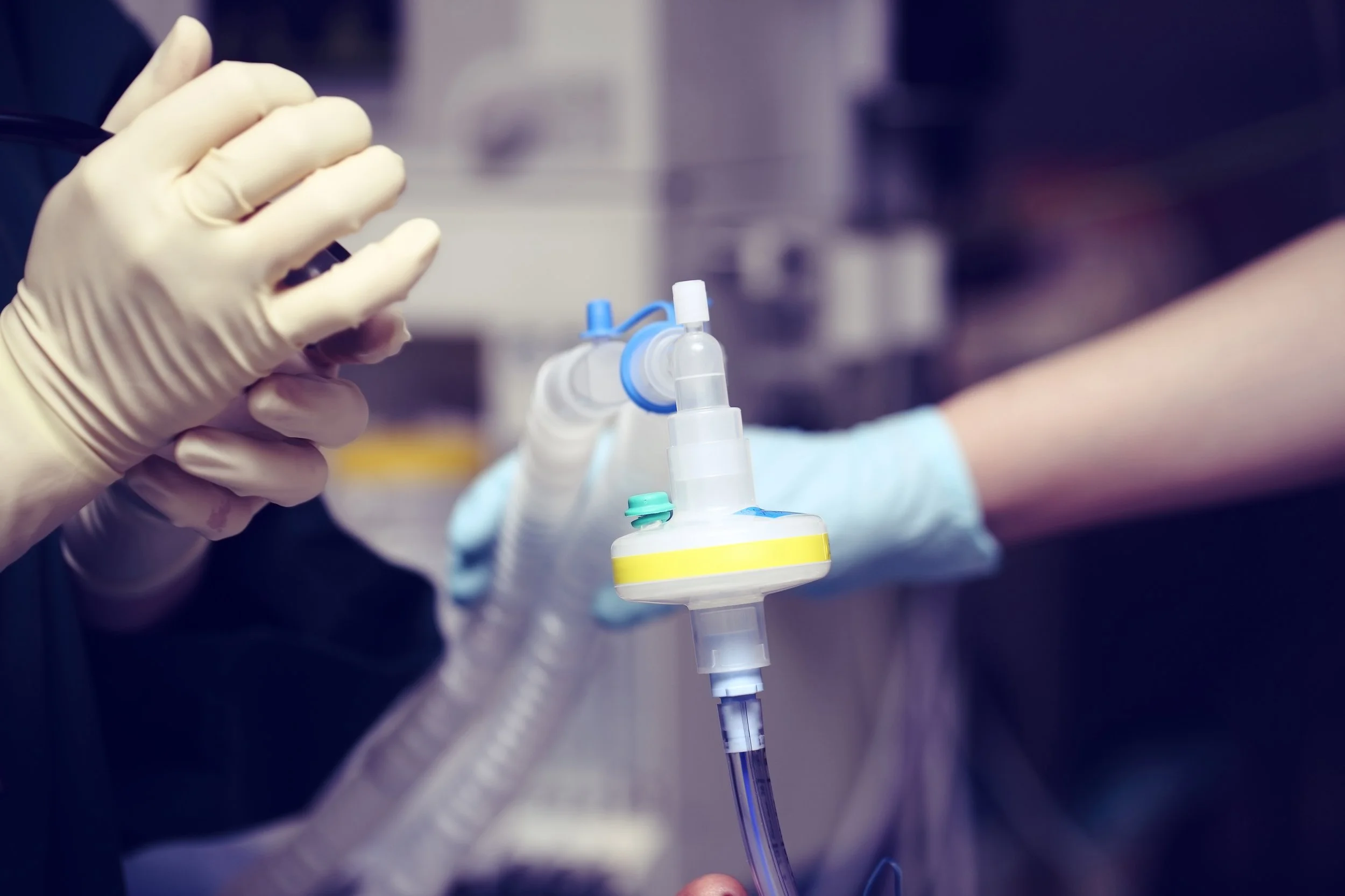 Close-up of a medical professional's gloved hands adjusting a mechanical ventilator in a hospital setting.