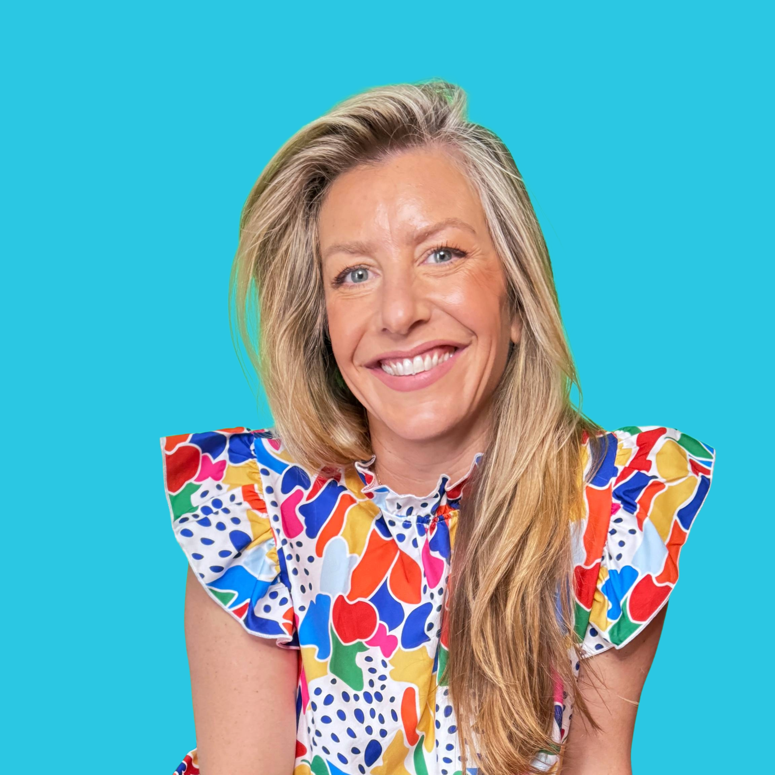 A woman with long blonde hair smiling, wearing a colorful, patterned dress with ruffled shoulders, against a bright blue background.