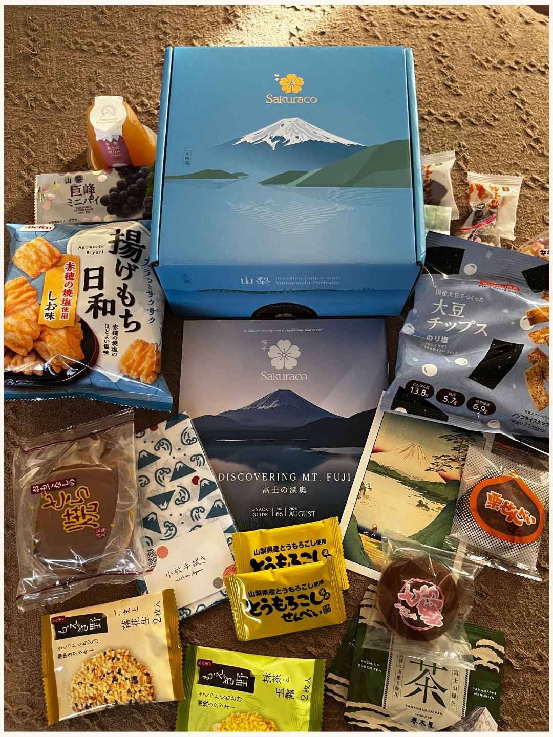 Full contents of the Sakuraco Discovering Mt. Fuji box laid out, snacks, tea, and postcard