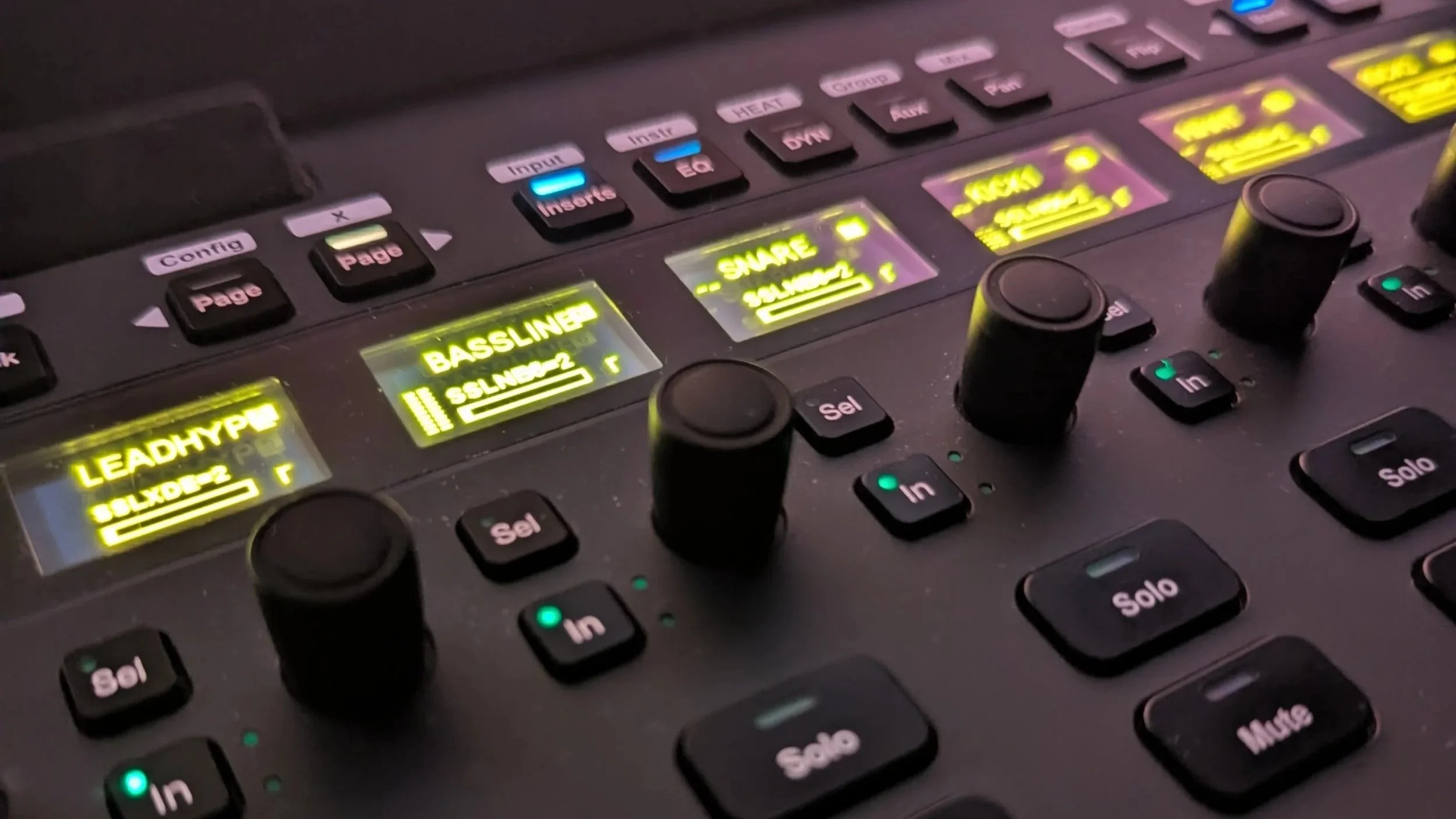 Close-up of professional audio control hardware with illuminated track labels, knobs, and mixing controls.